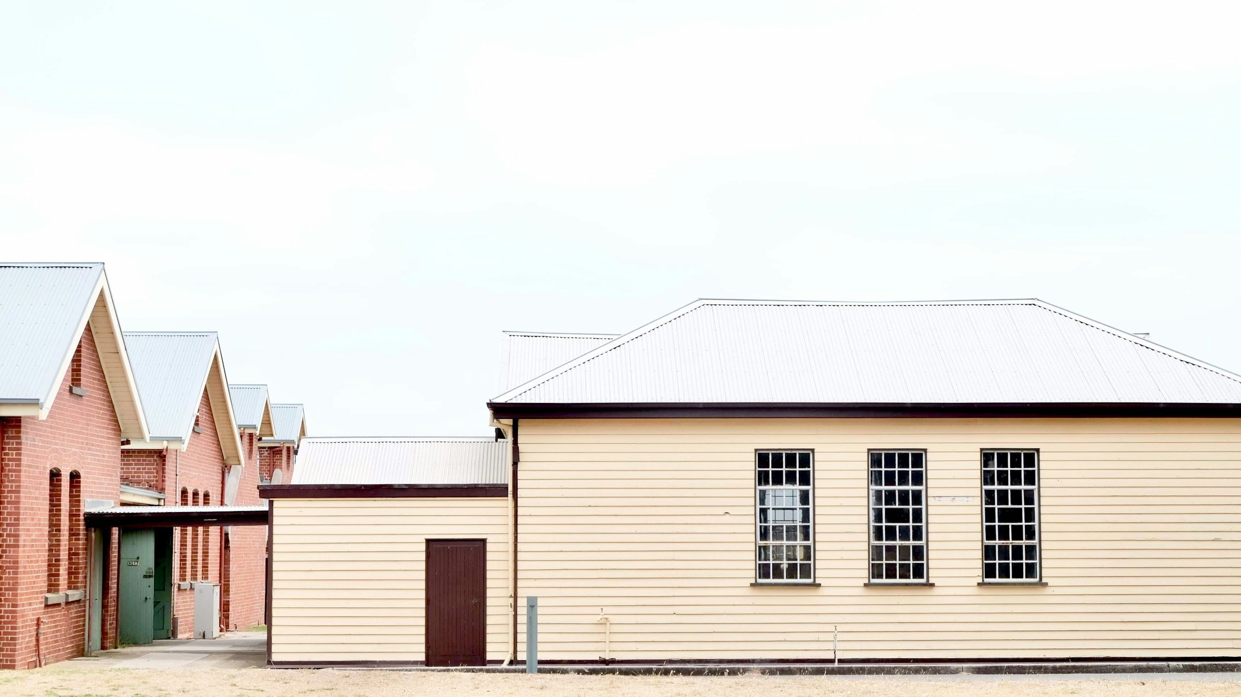Row of houses with brick and beige siding, white metal roofs, and multiple windows under a cloudy sky.