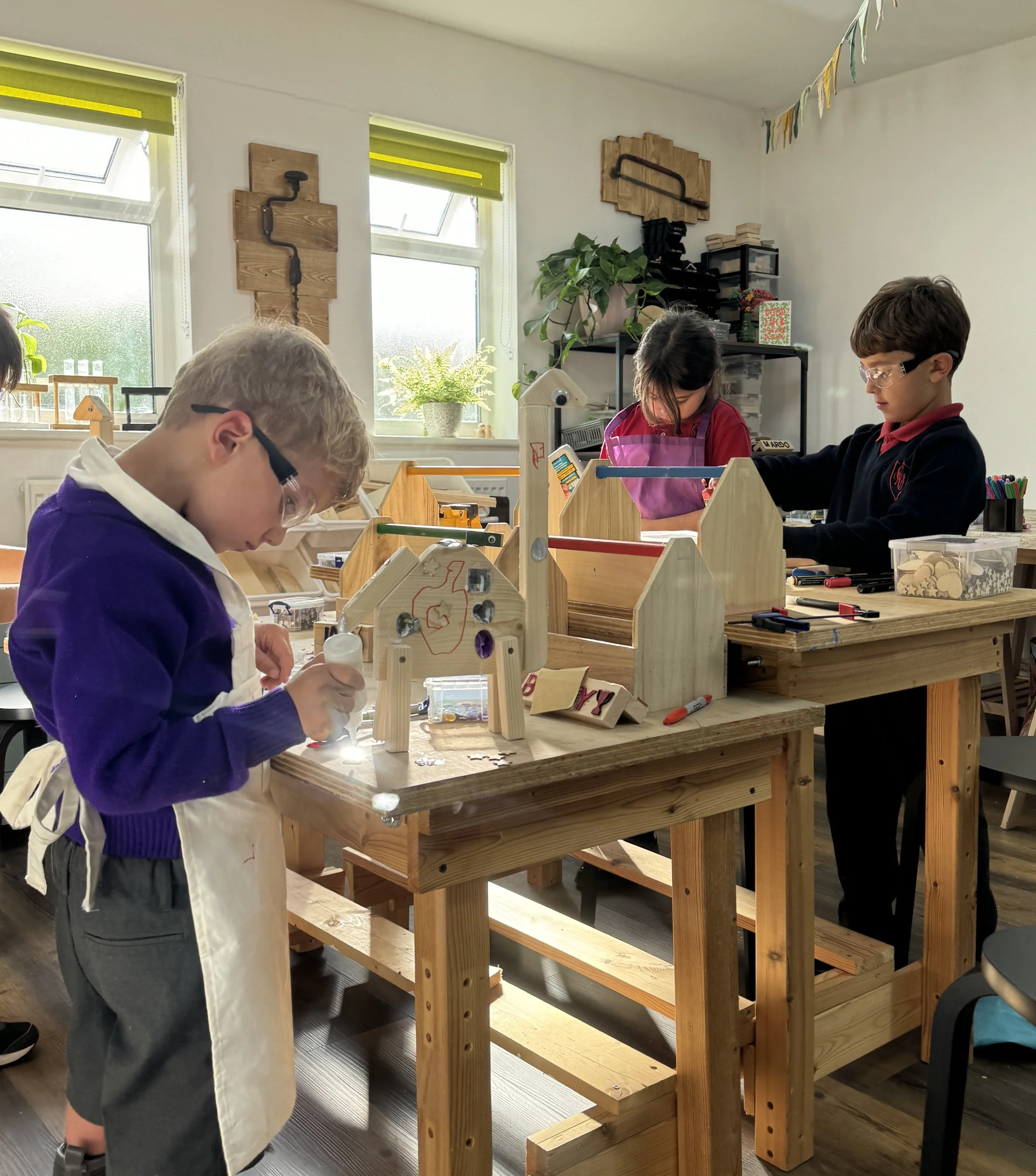 Three children working on projects at a woodworking workbench in a classroom.