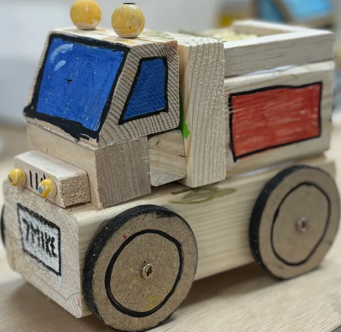 Wooden toy truck painted with blue windows and red side panel, with yellow wheels and a label reading 'TRUCK' on the front.