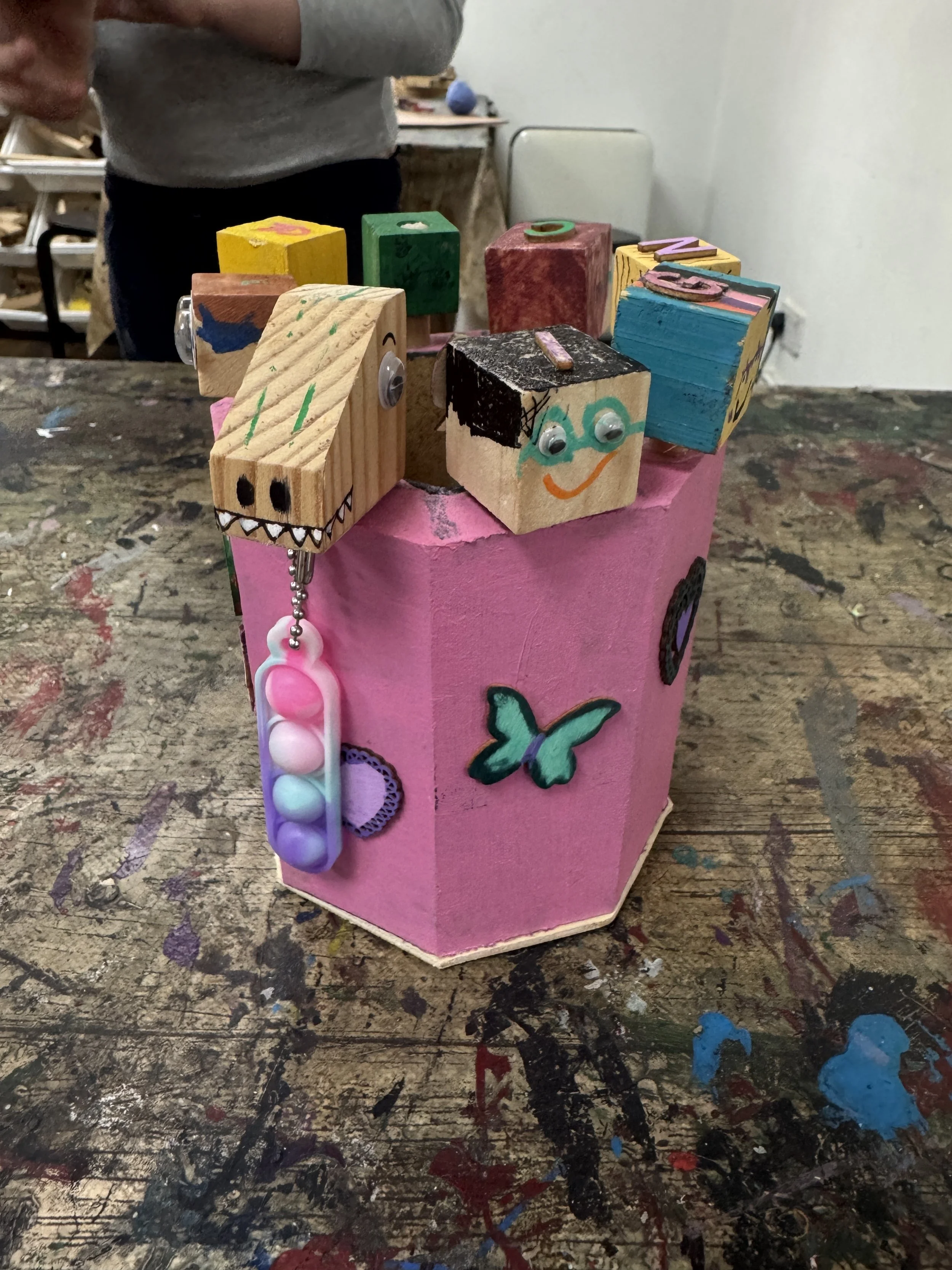 Colorful decorated wooden blocks arranged in a pink box on a painted and messy table.
