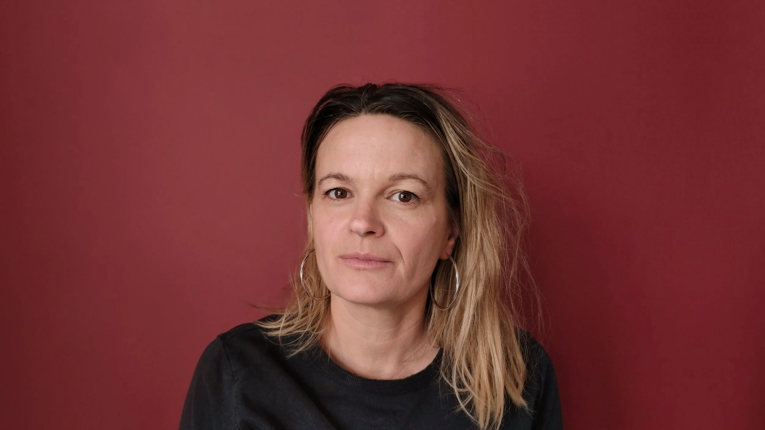 A headshot of professor Fiona Vera-Gray against a red background