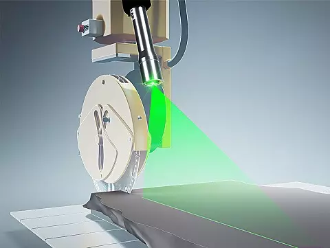 Medical laser device emitting a green laser beam onto a patient bed in a clinical setting.