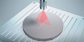 A kitchen sink with a circular glass cutting board and a red laser pointer directed at it.