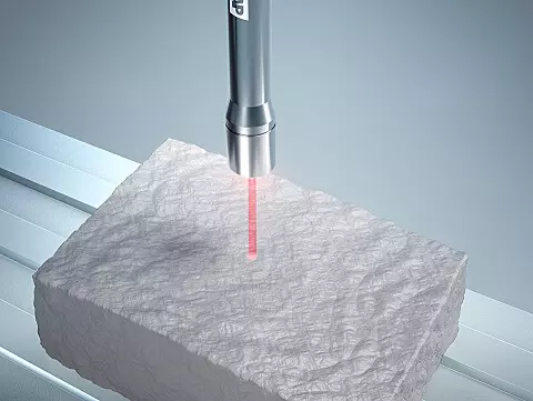 A scientific device emitting a red laser beam onto a textured white block in a laboratory setting.