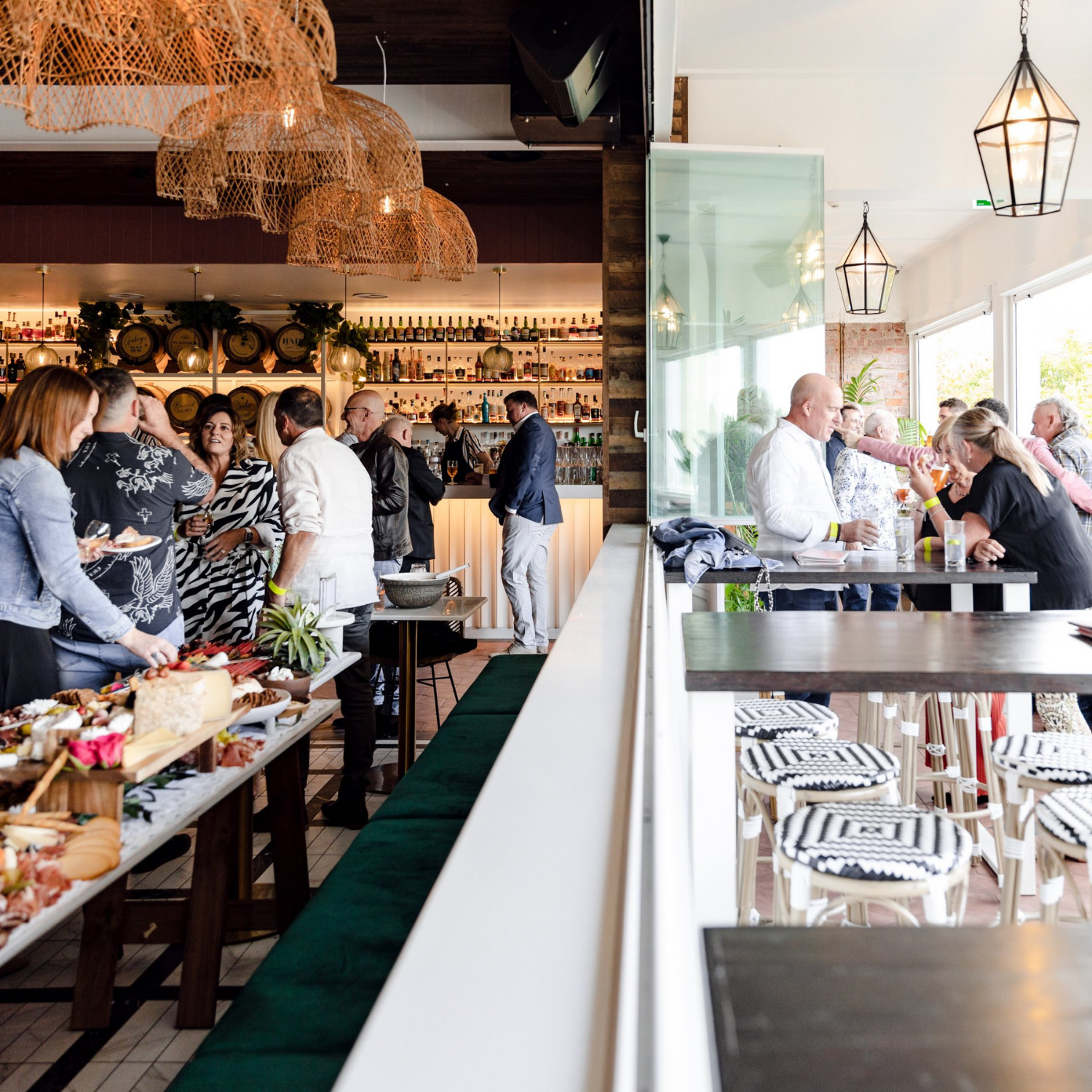 People socializing and enjoying food and drinks at a bar and dining area in a modern, stylish restaurant with indoor and outdoor seating.