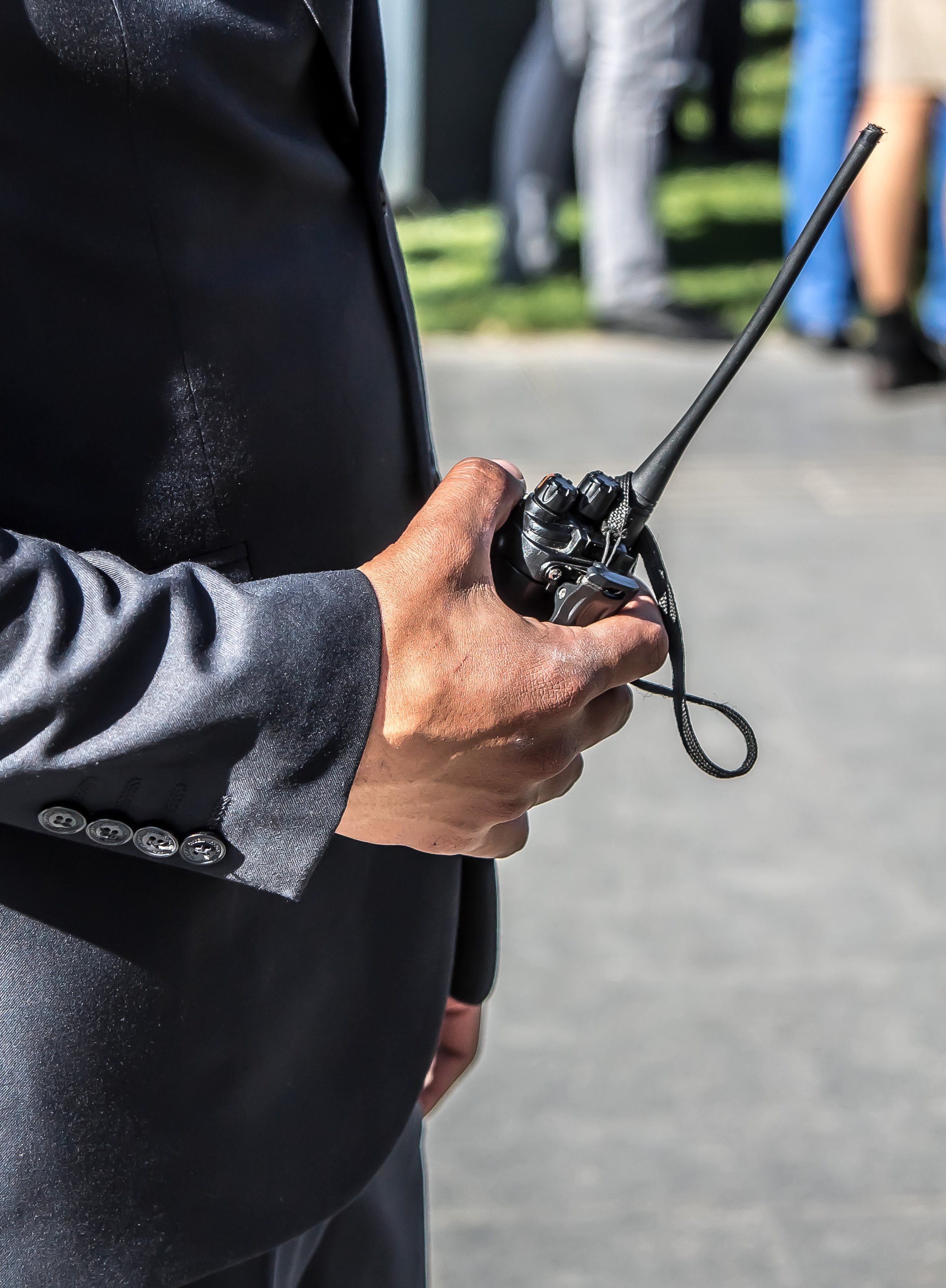 Close-up of a person wearing a black suit, holding a walkie-talkie with an antenna.