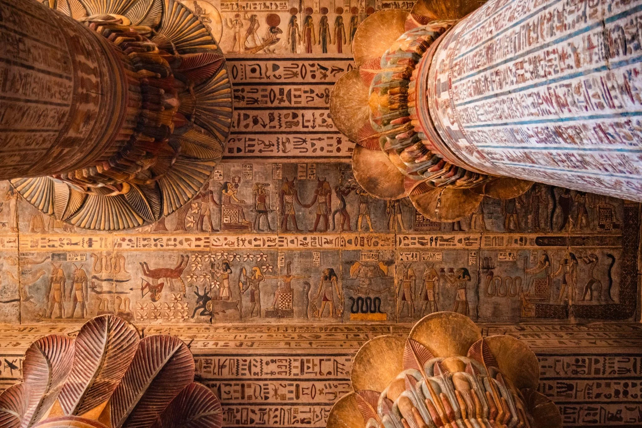 Ancient Egyptian hieroglyphs and artwork on a ceiling in Esna temple, with carved and painted stone artifacts in the foreground.