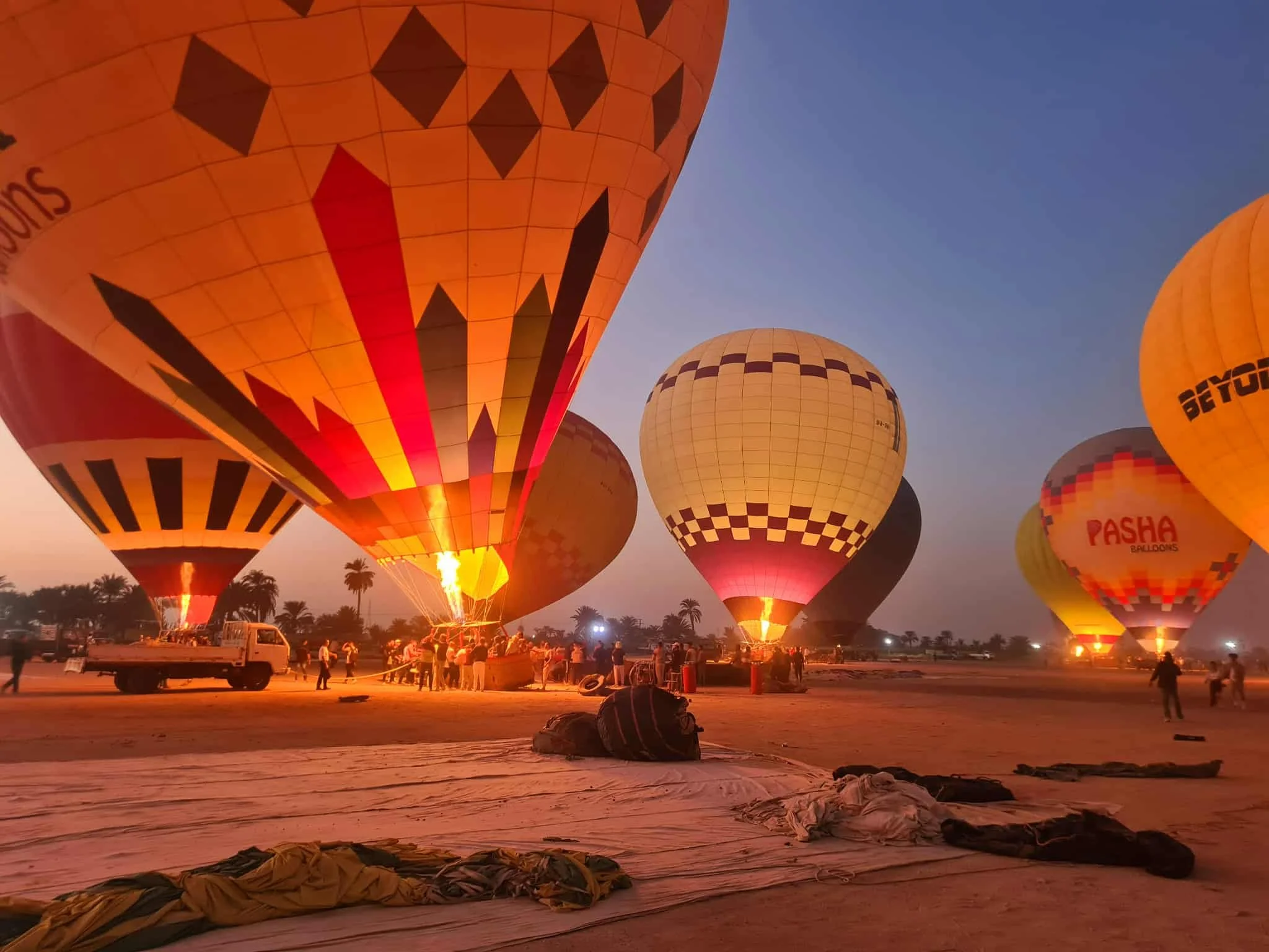 Multiple hot air balloons being prepared for lift in an open field at sunrise, with people and vehicles on the ground.