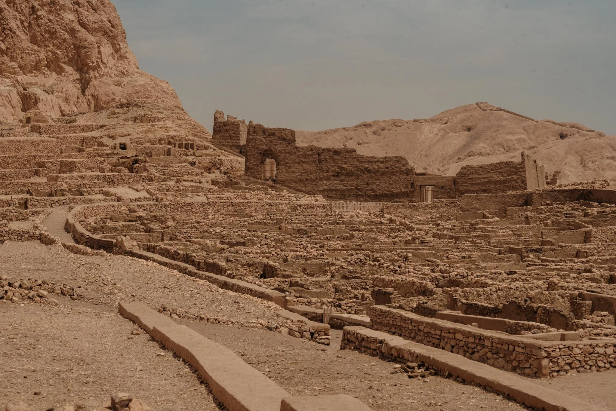 Valley of the scribes in Luxor an ancient archaeological site with stone ruins and terraces in a desert landscape under a cloudy sky.