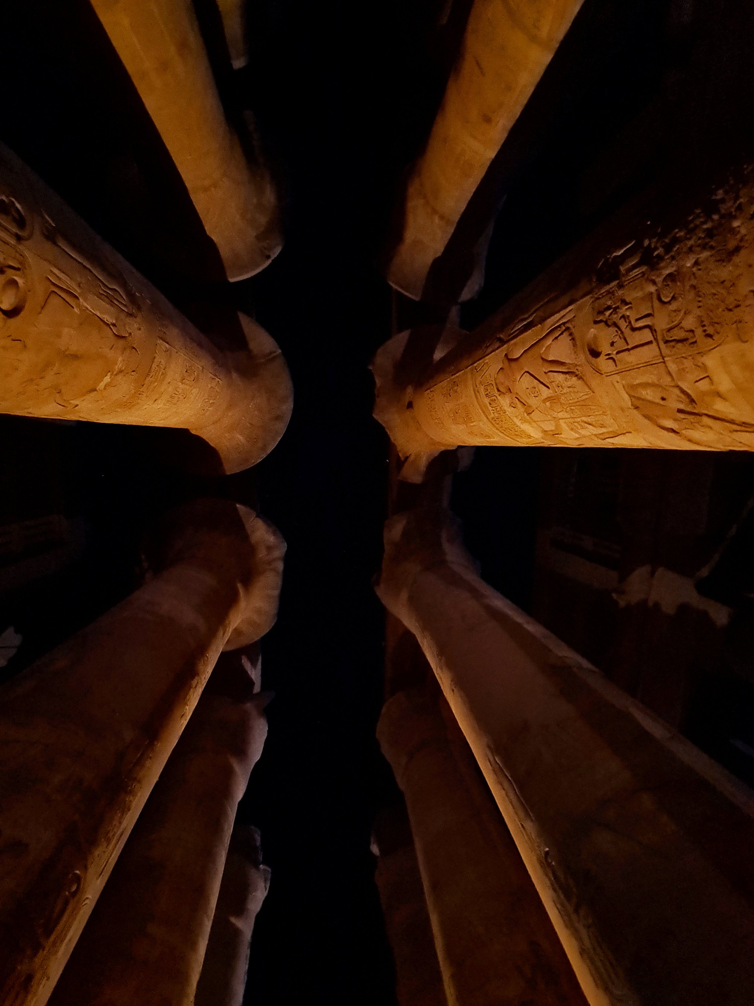 Close-up photo of ancient Egyptian hieroglyphics carved into two large stone columns at the Karnak Temple at night.