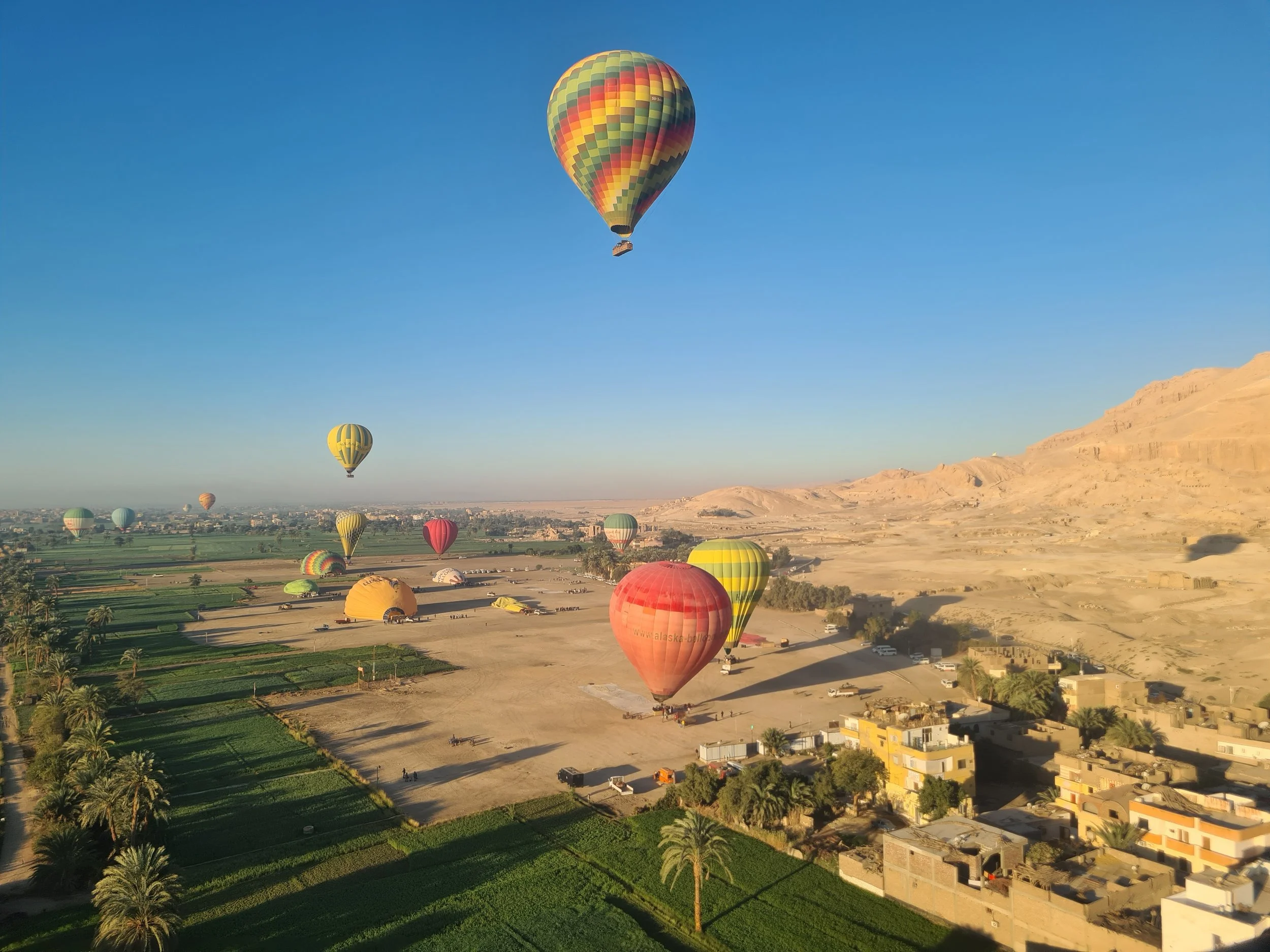 Hot air balloons flying over a desert landscape with mountains and green fields.