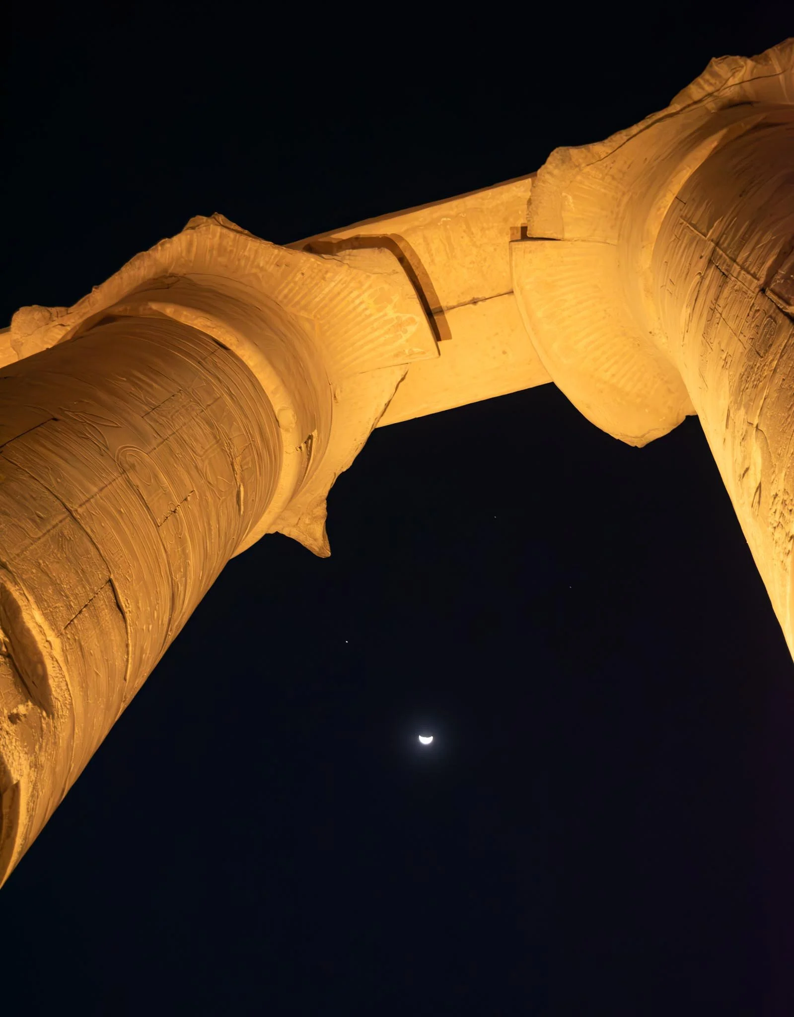 Night view of two large illuminated columns from below, with the crescent moon and a star visible in the dark sky.