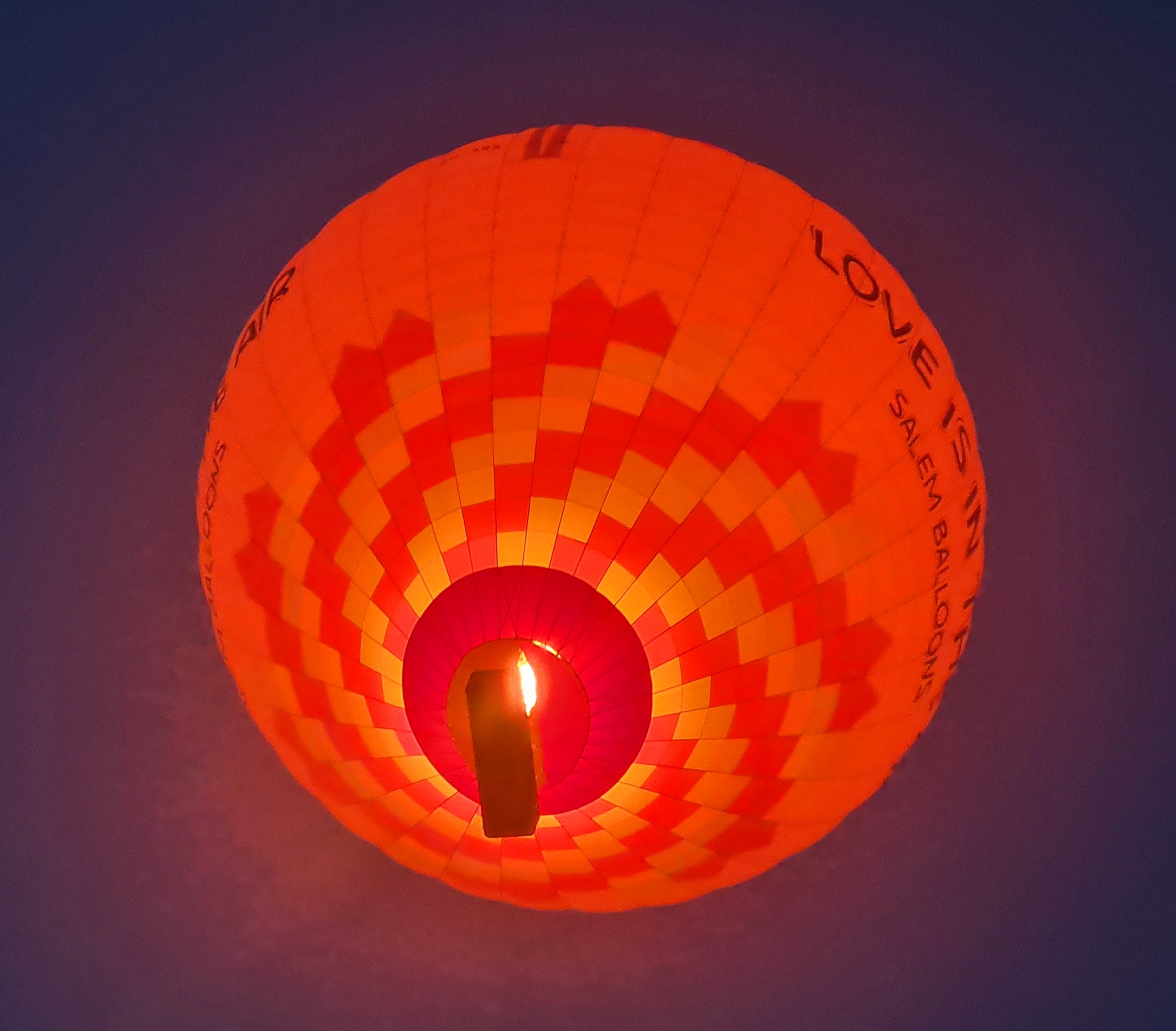 A brightly lit orange hot air balloon floating in the dark morning sky before sunrise in Luxor.