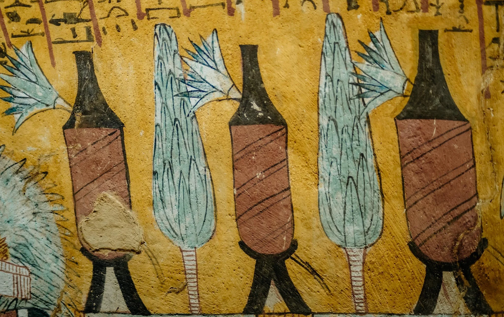 A mural with hand-drawn vases containing blue and green leaves, set against a yellow background with Egyptian hieroglyphs at the top.