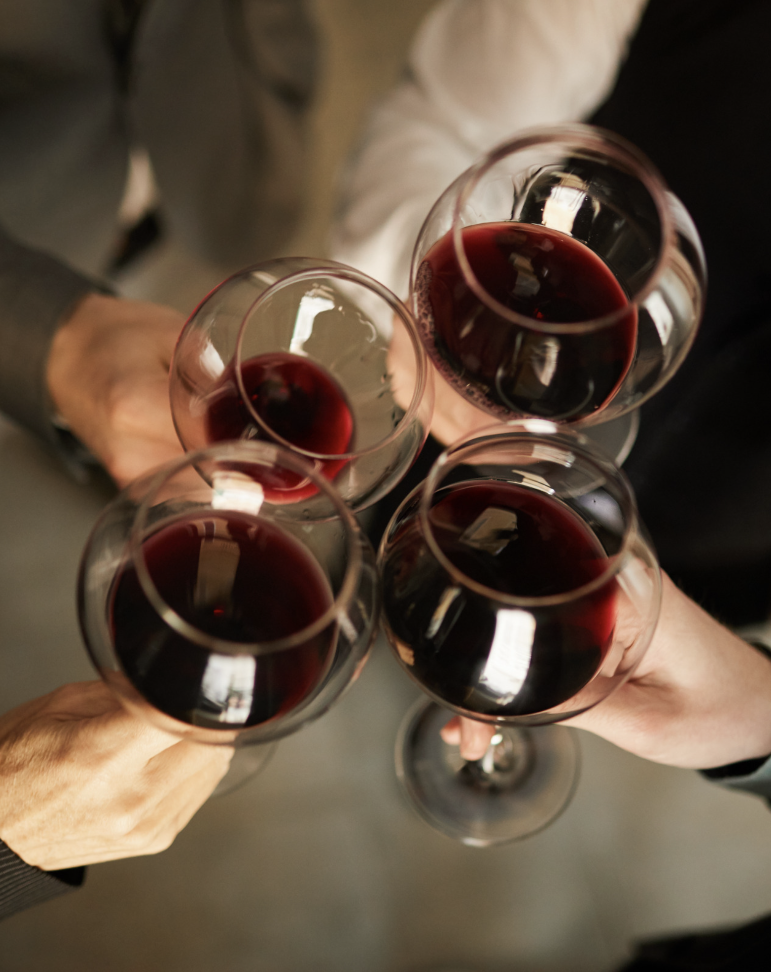 Multiple glasses of red wine held in a toast, viewed from above, with hands visible at the bottom of the image.