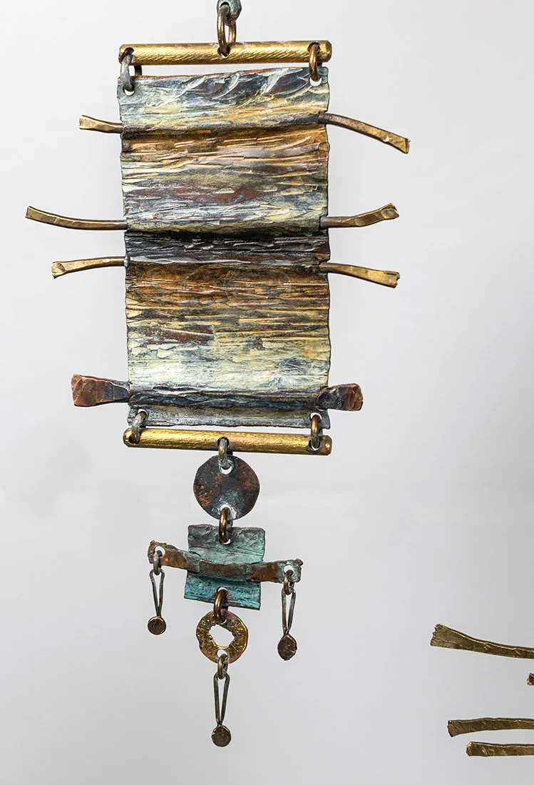 The panel chiselled and textured in copper and brass, the grain running like woven cloth, then crossed and pinned where the threads would meet.
