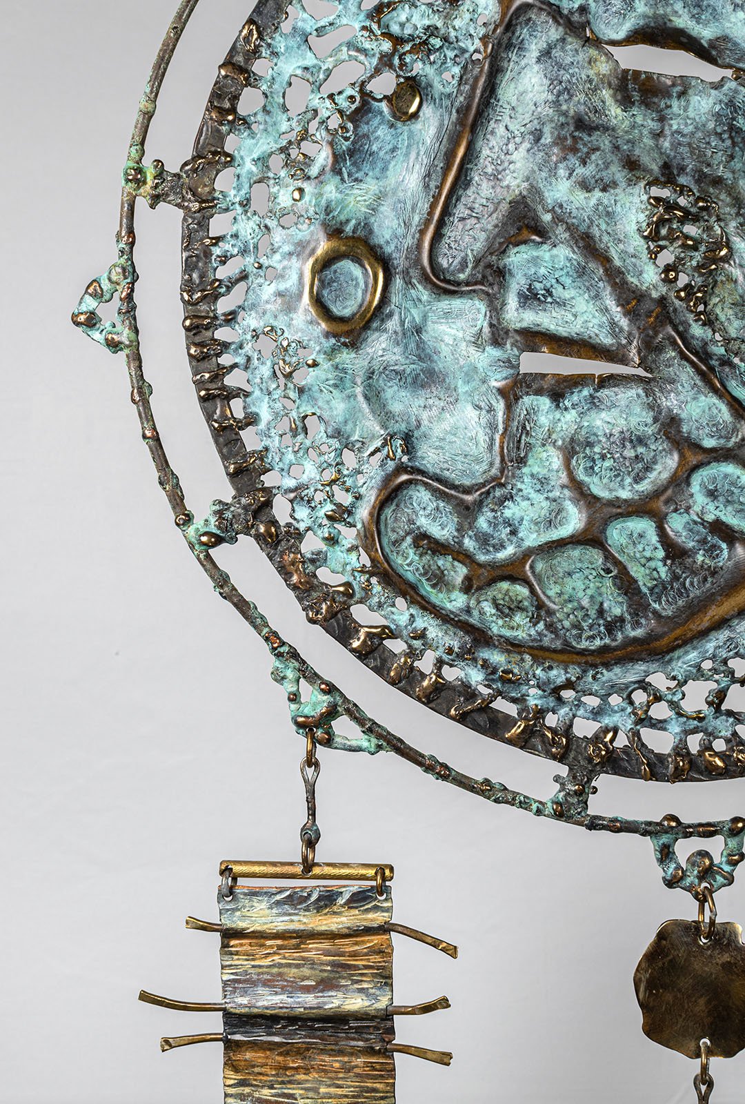 A disc of smithed brass, raised by hand, then ornamented. The field is woven, not drawn: verdigris patina is layered and applied to the metal in stages, the way lines of wool are laid into the loom to build a tapestry palette of colours.