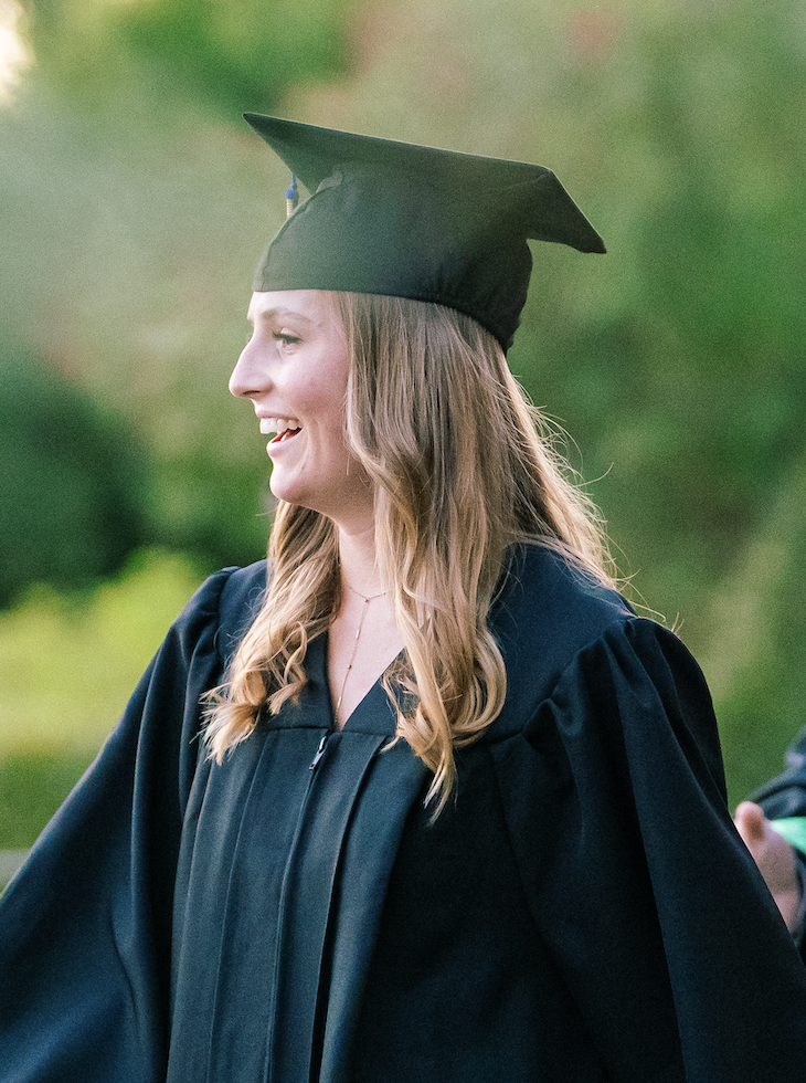 Jeune femme souriante en robe de graduation et bonnet, lors d'une cérémonie de remise de diplômes.