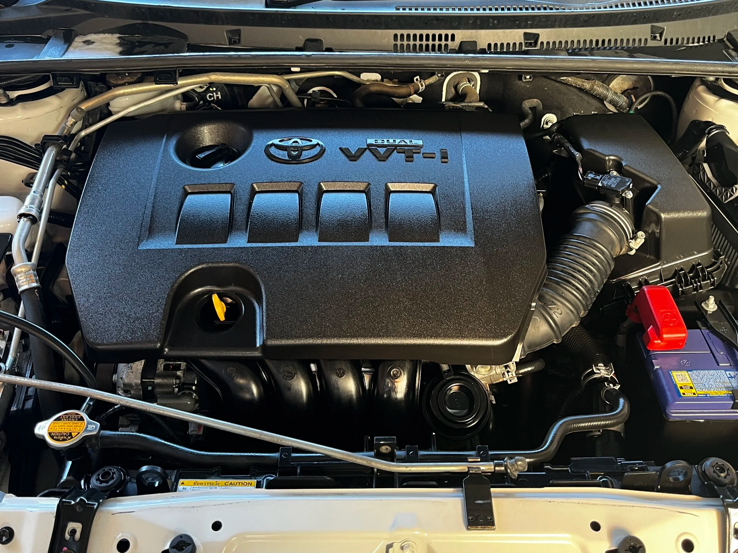 Toyota engine bay with VVT-i dual logo on the engine cover and various hoses and components visible.