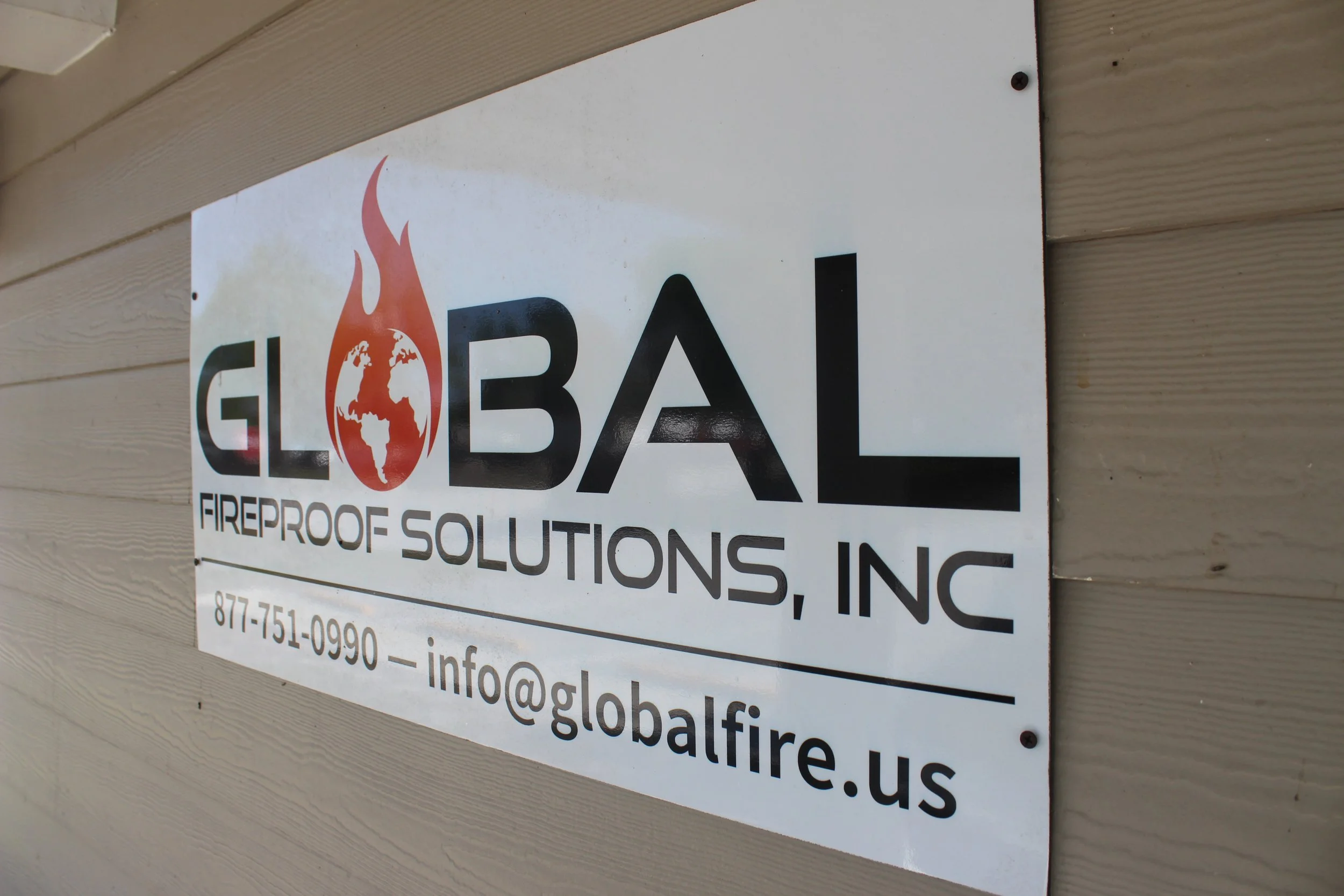 Sign for Global Fire Protection Solutions Inc. attached to a beige wooden wall, displaying website and contact information.