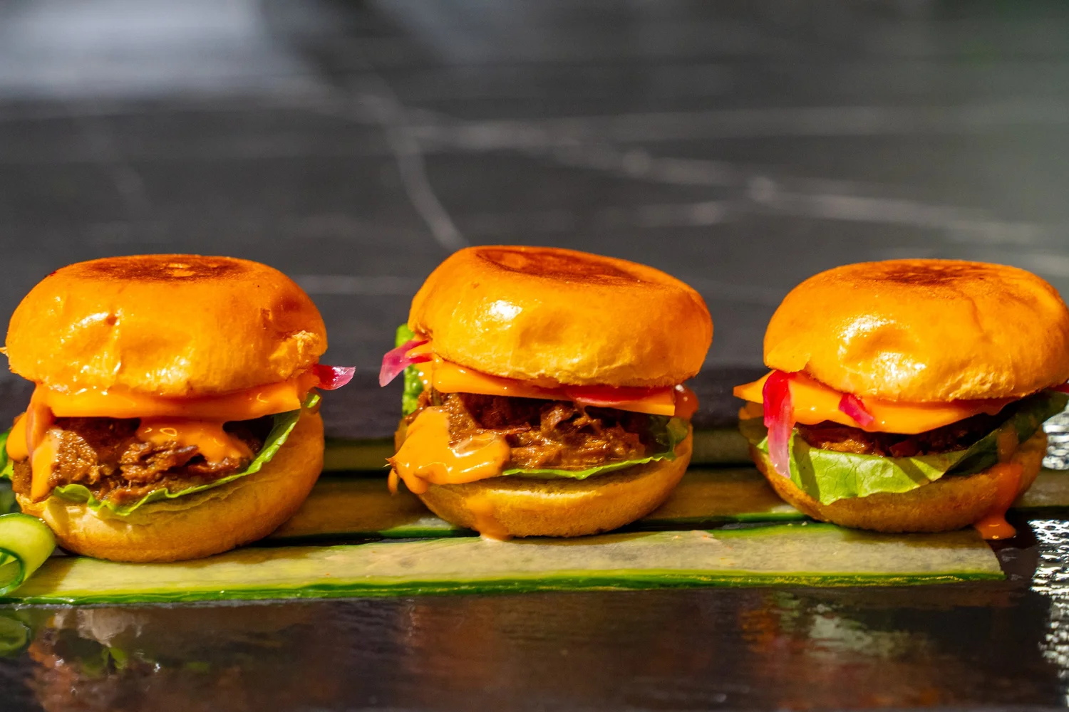 Three miniature burgers presented on a serving board