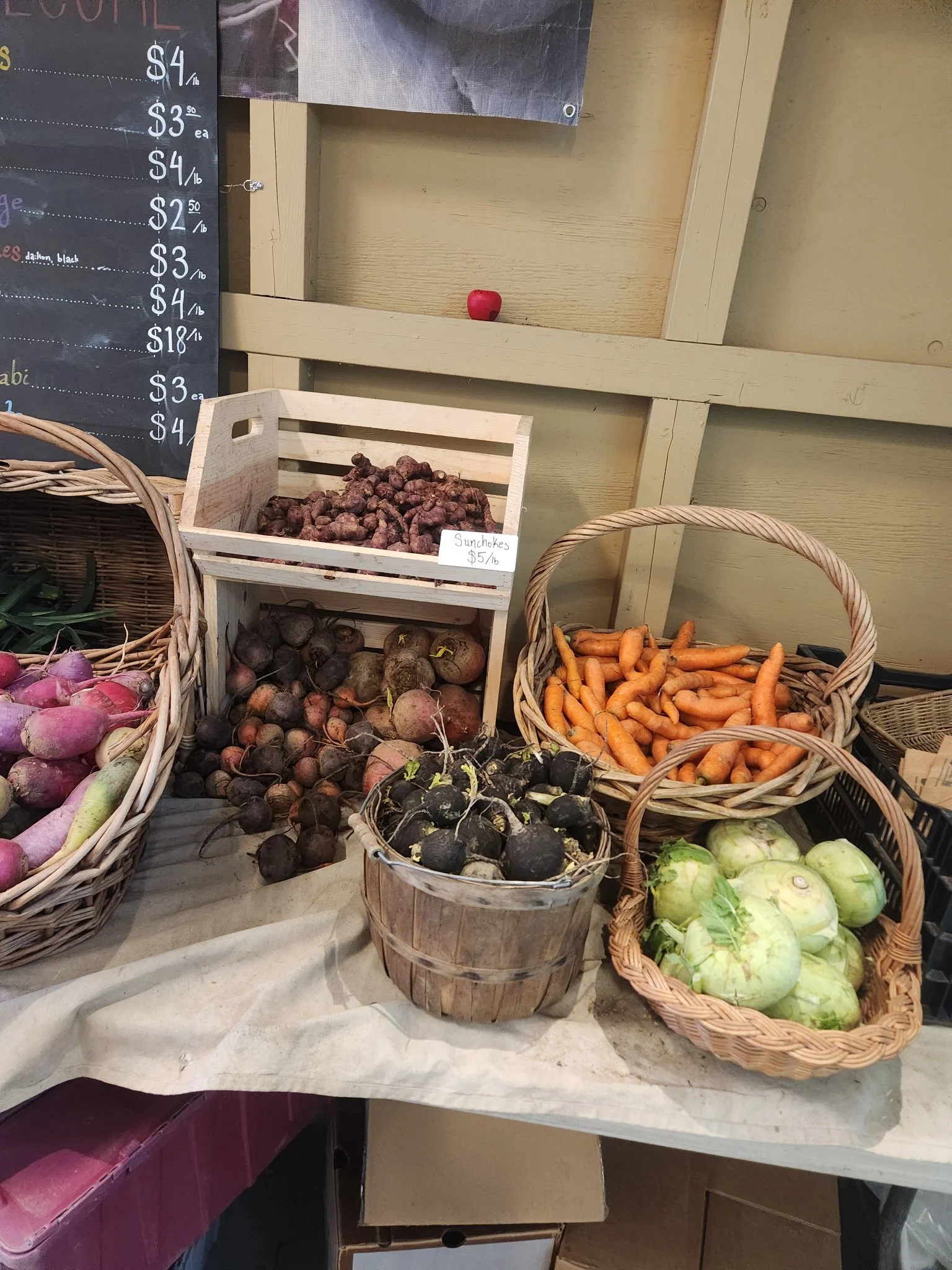 Various fresh vegetables in baskets at a farmers market, including carrots, beets, turnips, and kohlrabi.