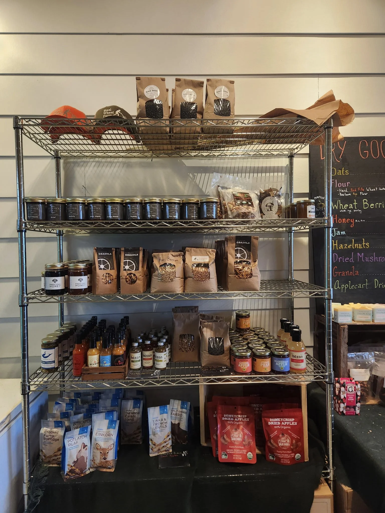 A metal shelving unit filled with various packaged food products in a store, with a blackboard menu on the right side listing different foods.