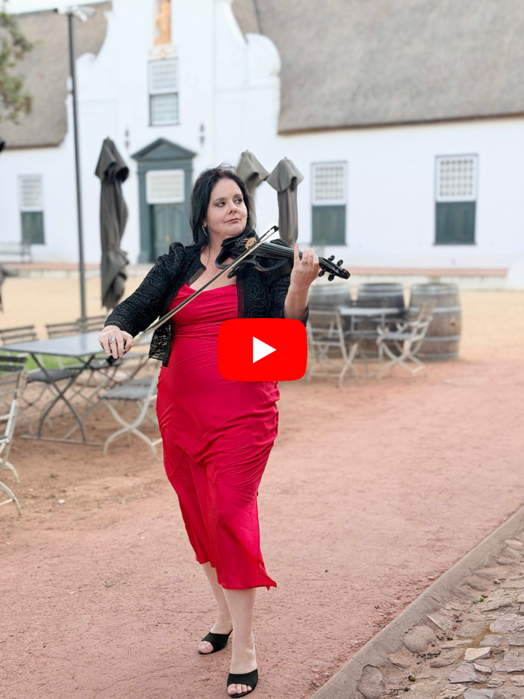Larah Eksteen playing the violin outdoors at Groot Constantia in a courtyard with historic buildings and empty tables and chairs.