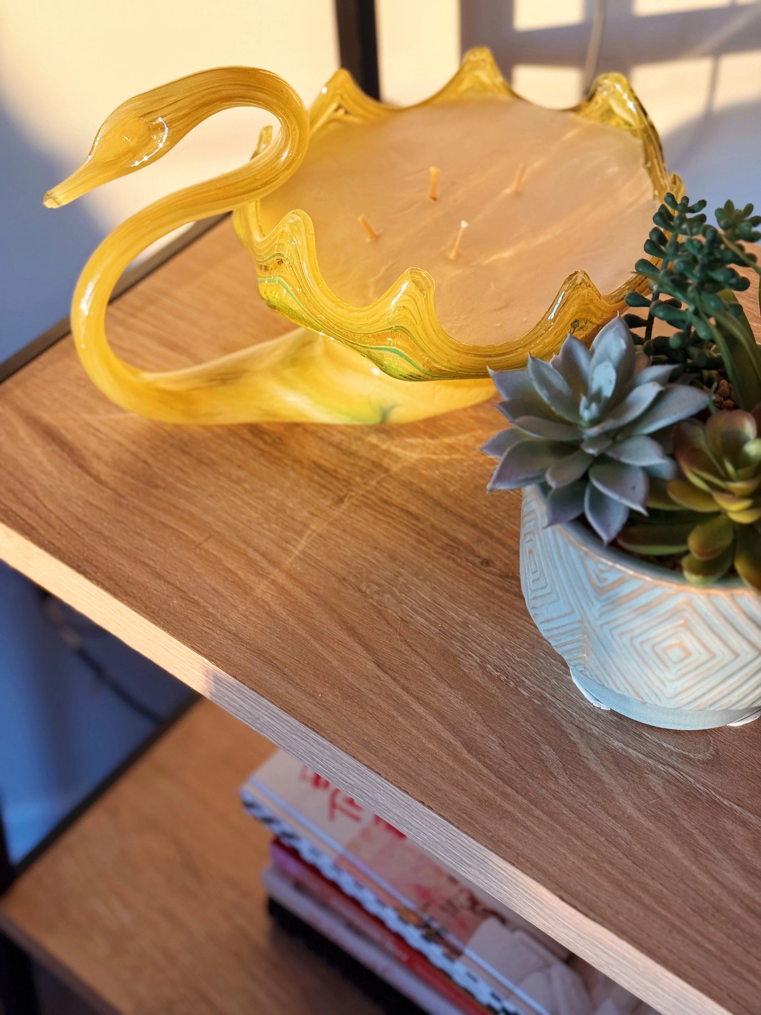 Yellow glass candle holder on wooden surface next to potted succulent plant
