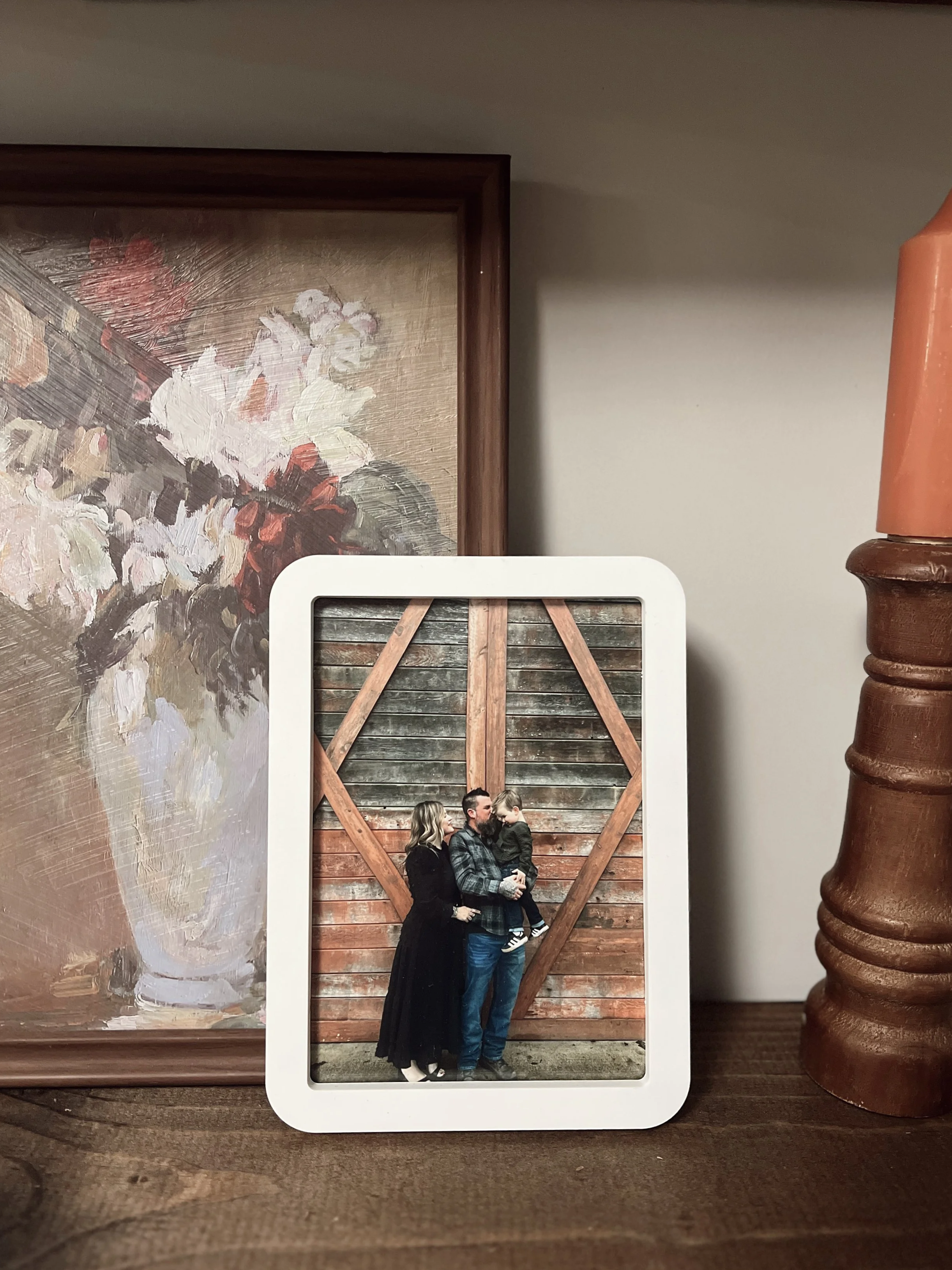 A framed photograph of a family of three standing in front of a wooden barn door, with the woman, man, and young child all facing each other closely.