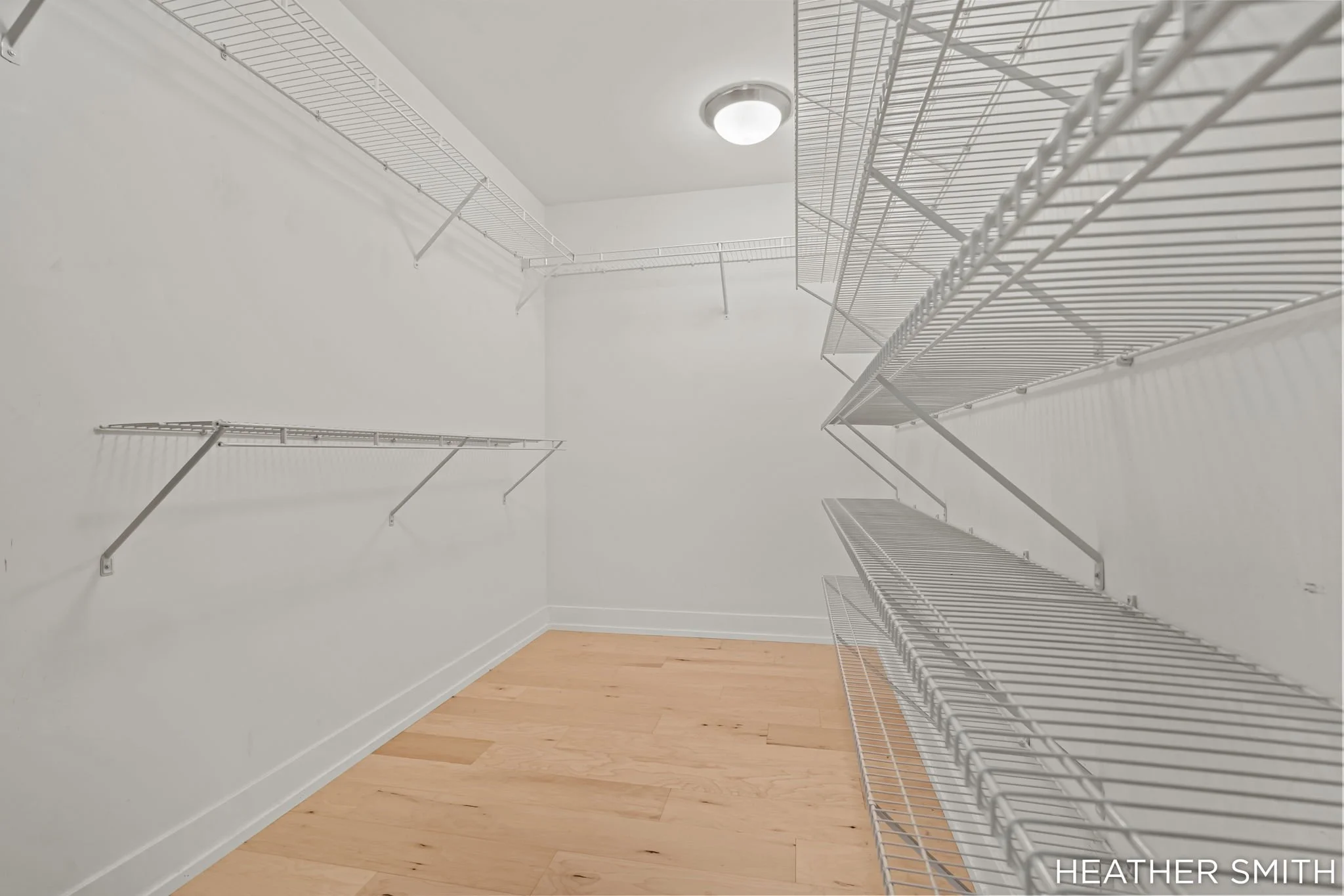 Empty walk-in closet with white wire shelves on light-colored wood floor, white walls, and ceiling with a dome light.