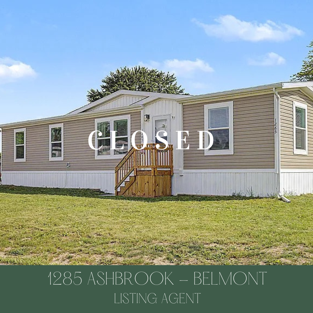 Single-story mobile home with beige siding and white trim, showing a small wooden front porch. The house is marked as 'CLOSED' and located at 1285 Ashbrook in Belmont, listed by a listing agent. The sky is blue with some clouds.