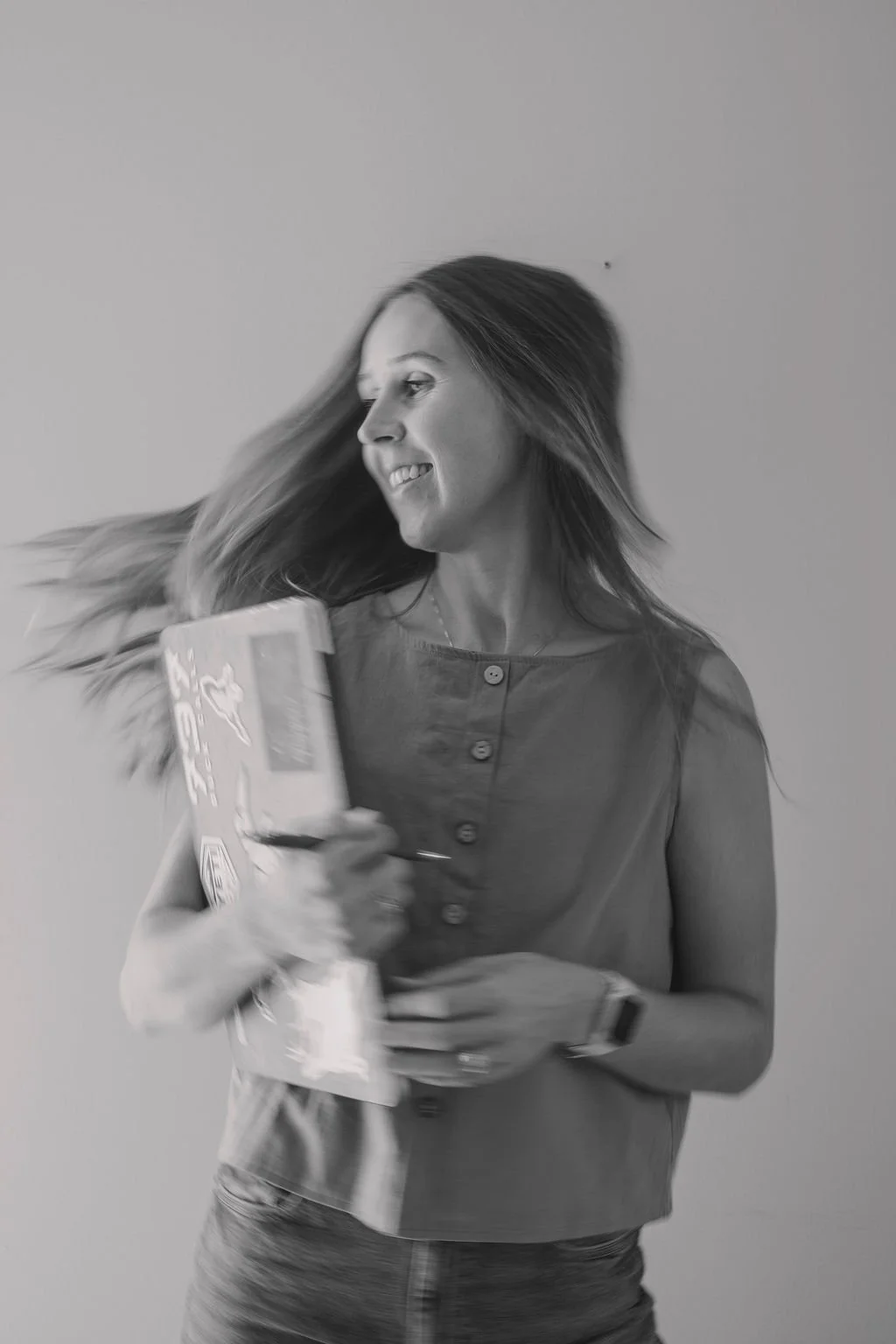 A woman with long hair smiling and looking to the side, holding a box of snacks or cereal in her left hand, against a plain background.