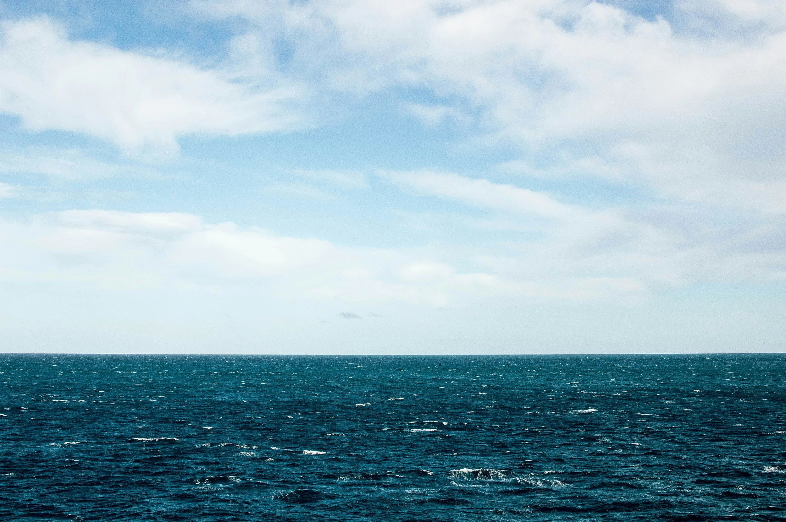 A wide view of the ocean with rippling water under a partly cloudy sky.