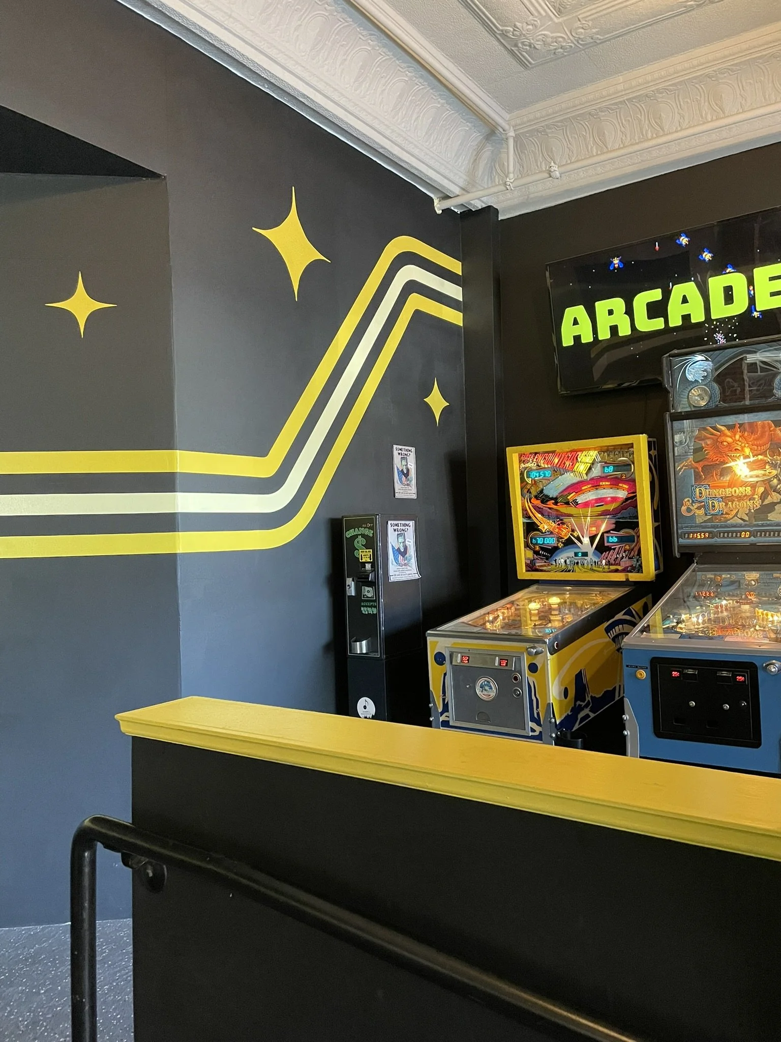 Arcade area with pinball machines, a blue and yellow color theme, and a black wall with yellow star decorations.