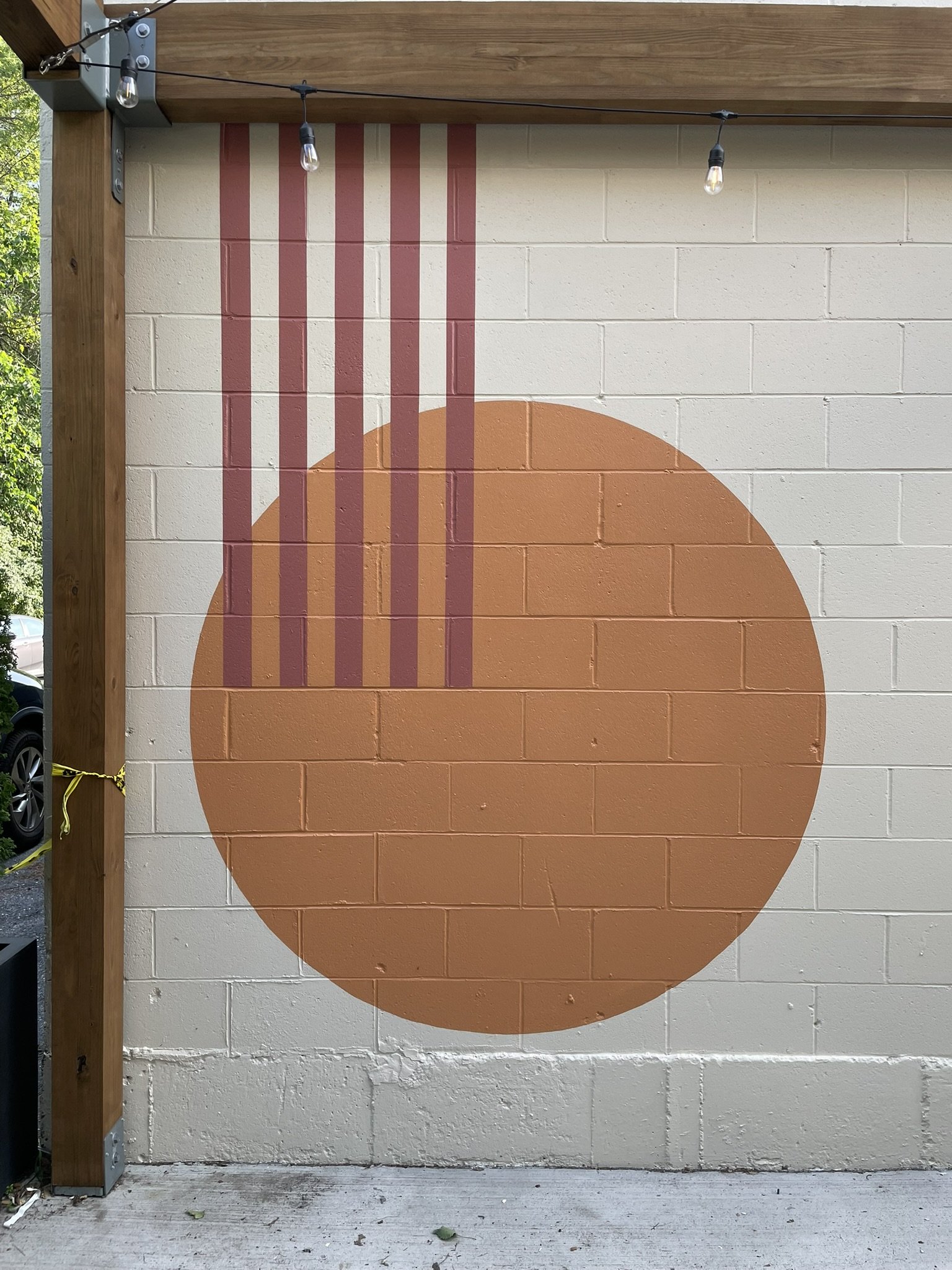 A mural on a brick wall featuring an orange circle with vertical red lines extending from the top of the circle to the top of the wall