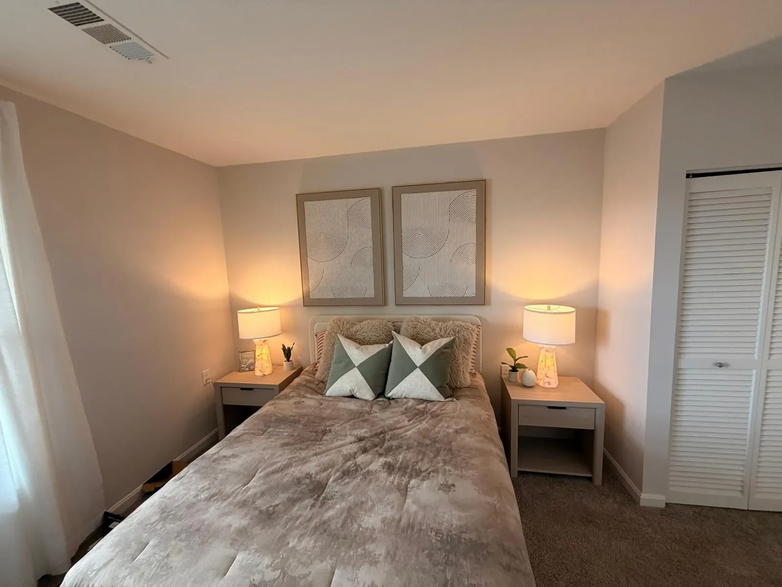 A bedroom with a bed, two nightstands with lamps, wall art, and decorative pillows.