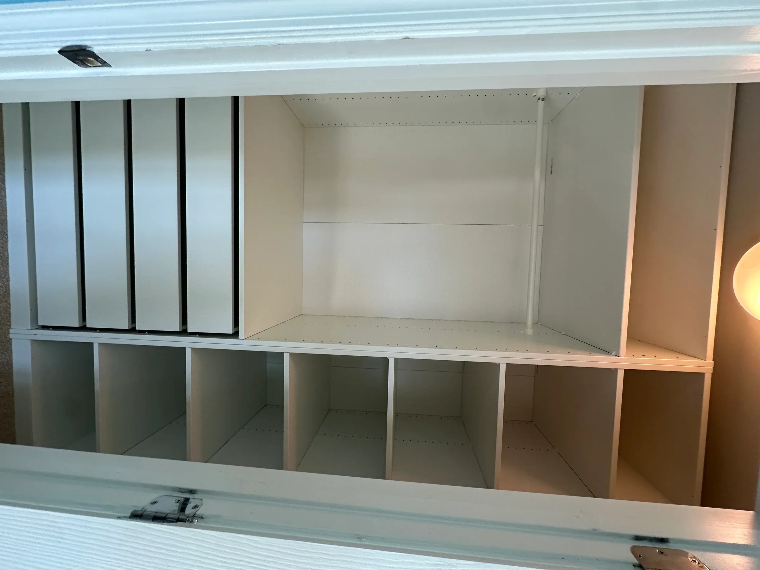 Empty white bookshelf with multiple compartments and black vertical dividers, inside a room with beige walls.