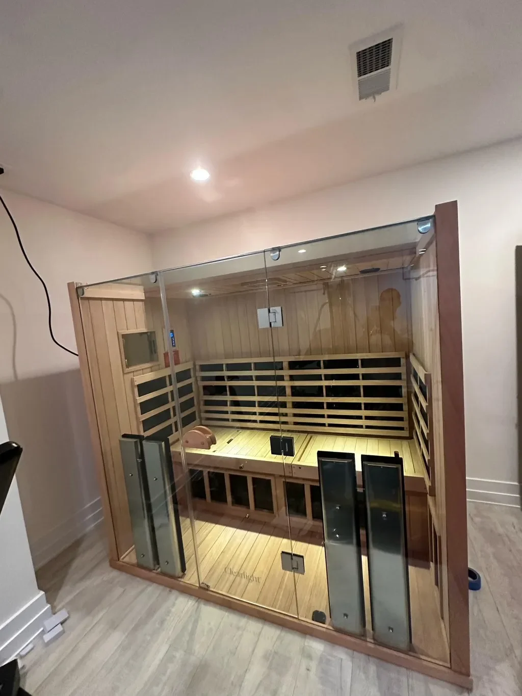 Indoor infrared sauna with glass walls, wooden interior, and a small heating unit inside.