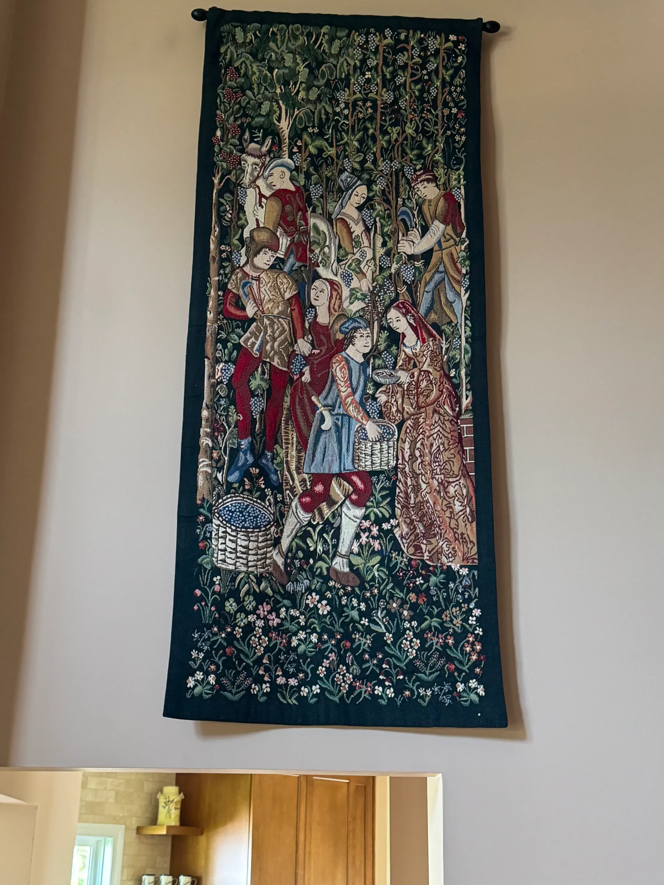 A tapestry depicting a historical or biblical scene with several people, including a man in armor and others in traditional clothing, surrounded by a flowering garden.