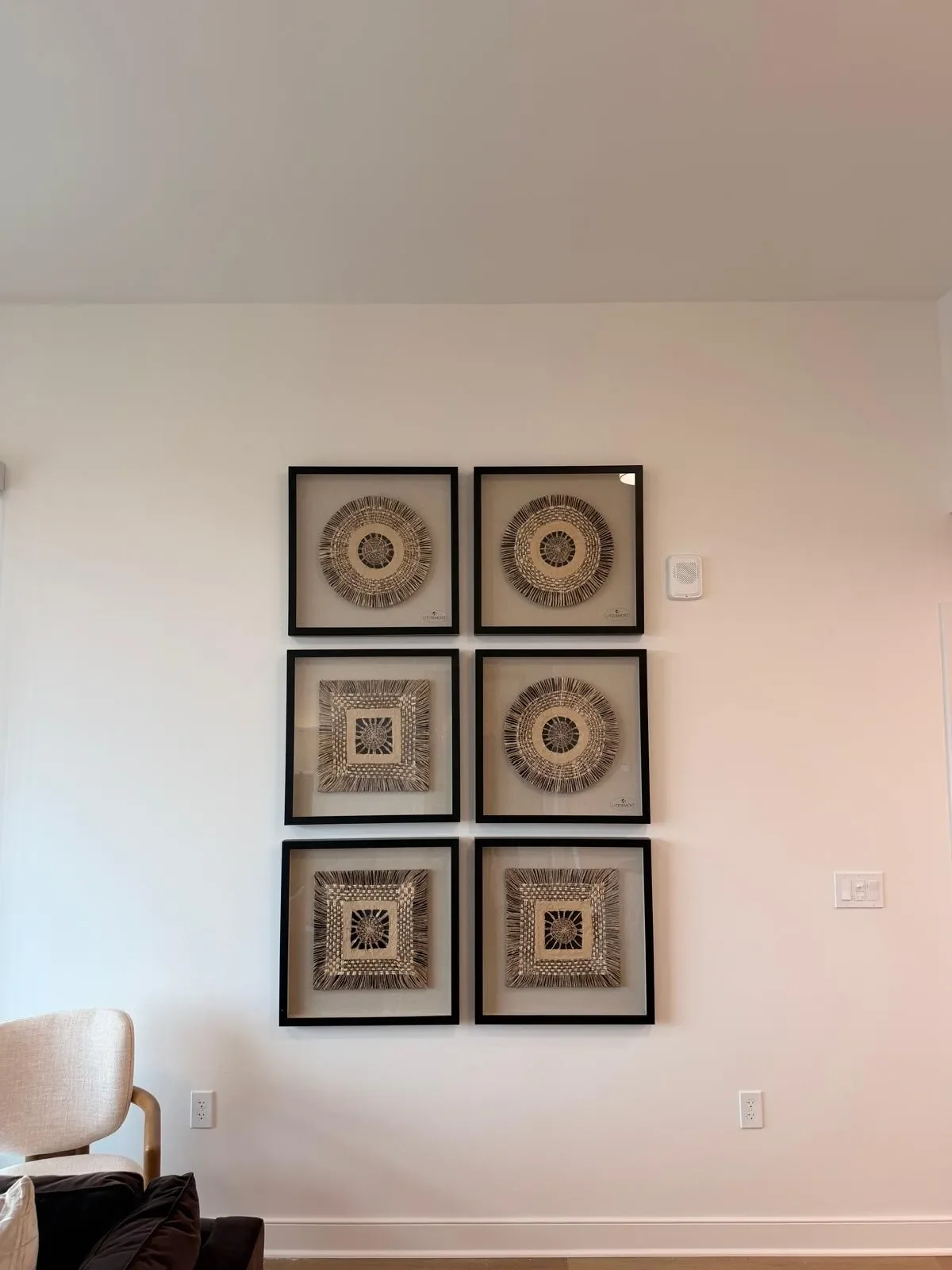 Six framed pieces of art featuring circular and square intricate designs are arranged in a grid on a white wall.