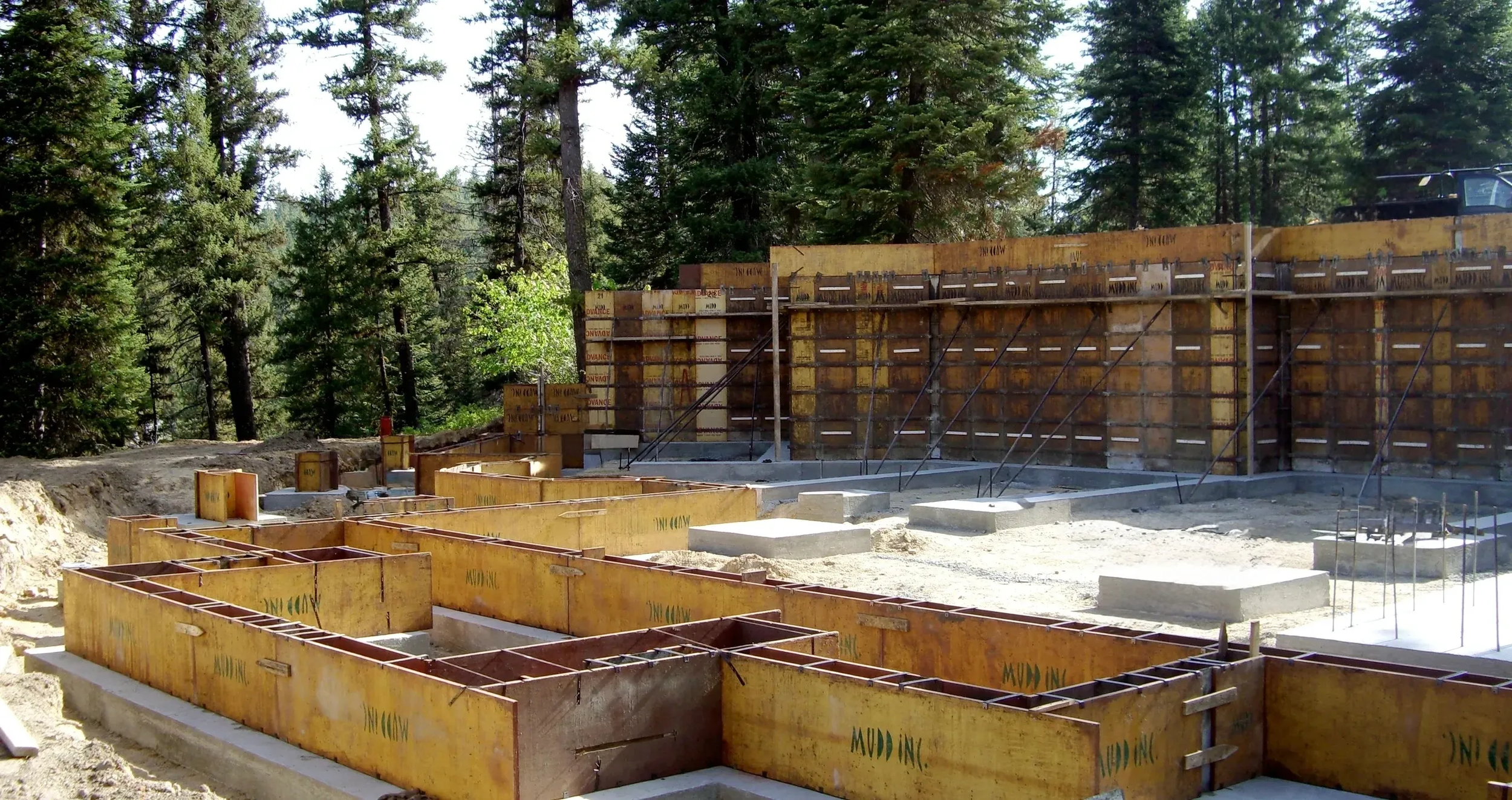 Construction site with formwork and rebar set for a building foundation, surrounded by trees and forest.