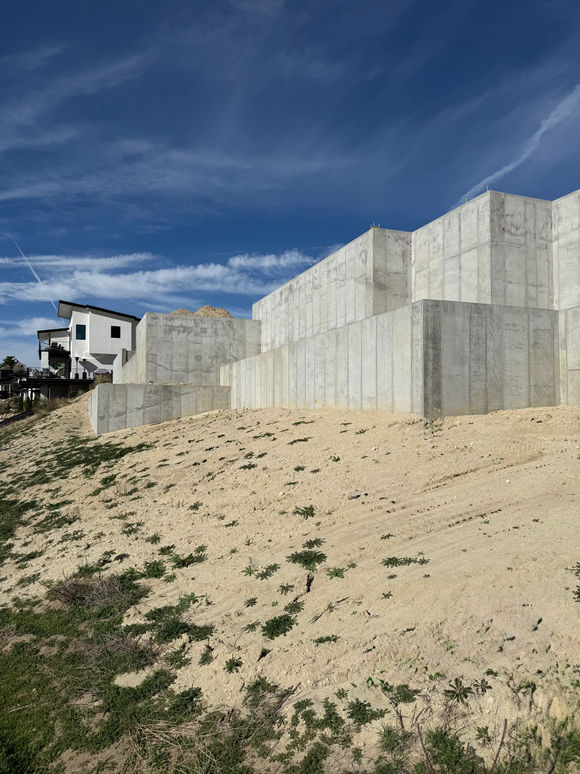 A modern house with a white exterior and black accents built into sand dunes on a sunny day with blue sky and wispy clouds.