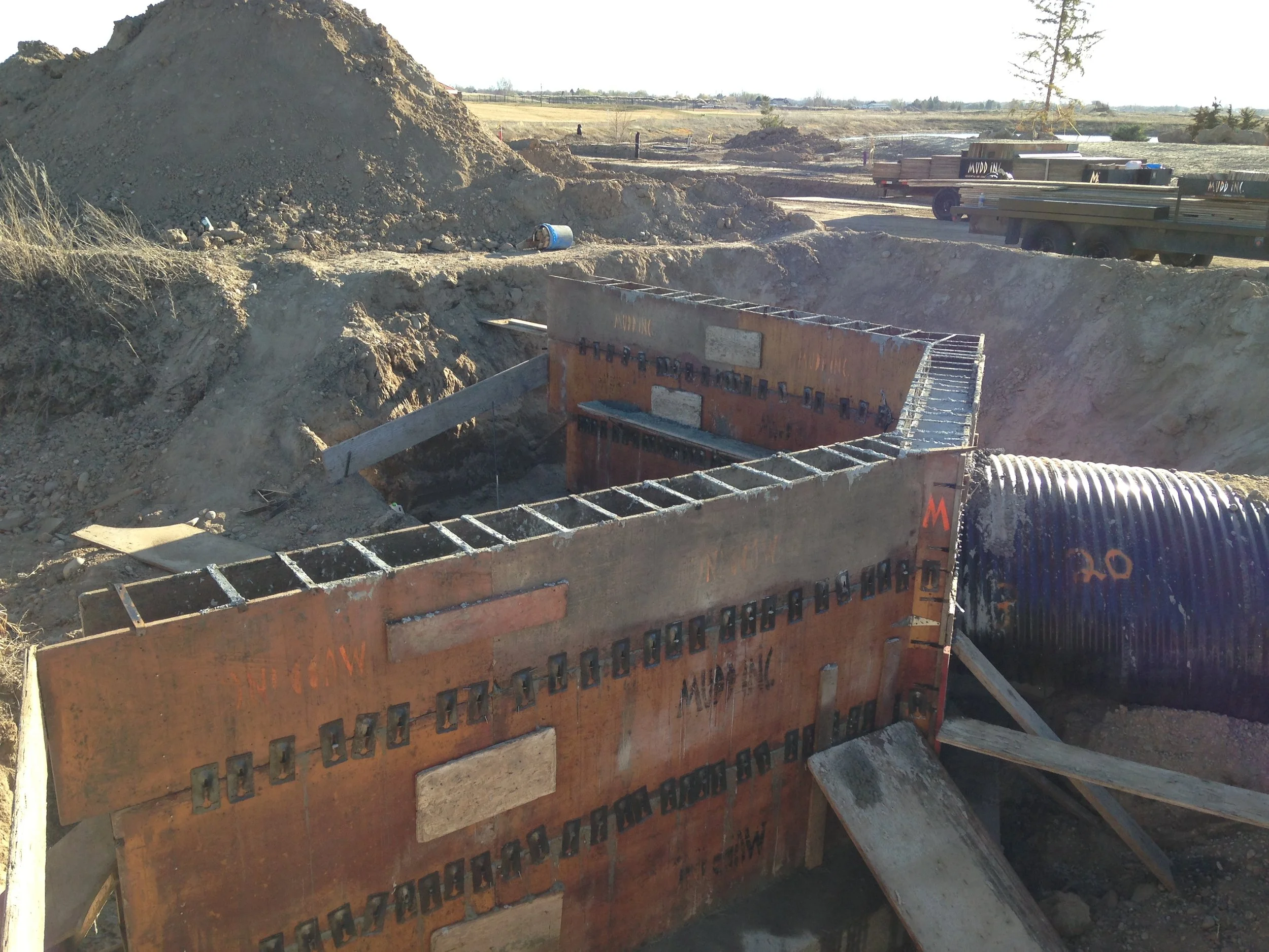 Construction site with large orange concrete form, dirt pile, and construction equipment in the background.