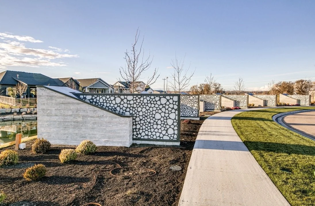 Modern concrete fence with circular cutout design alongside a curved sidewalk in a suburban neighborhood.