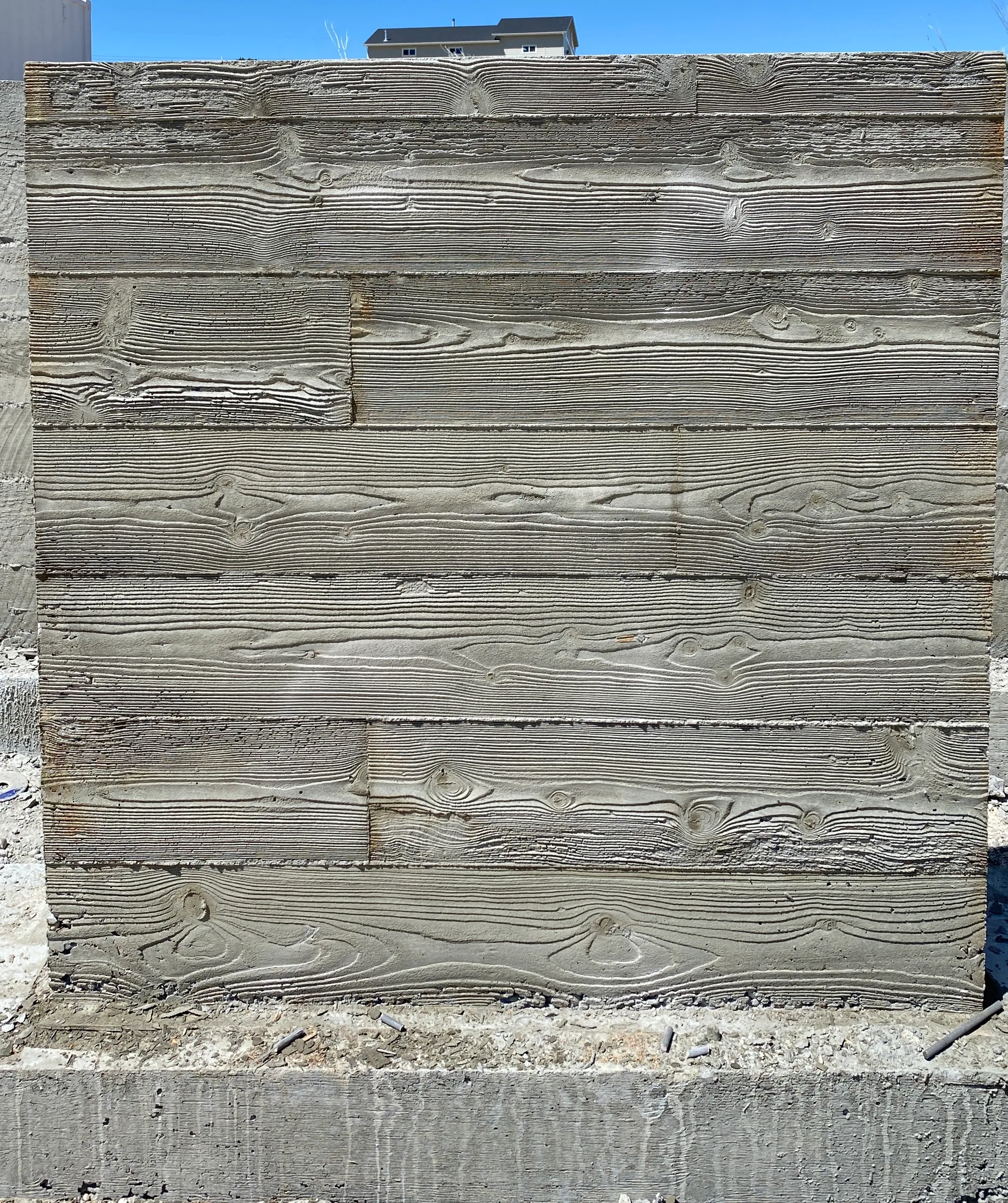 Wooden planks arranged vertically in a wall with a house seen in the background.