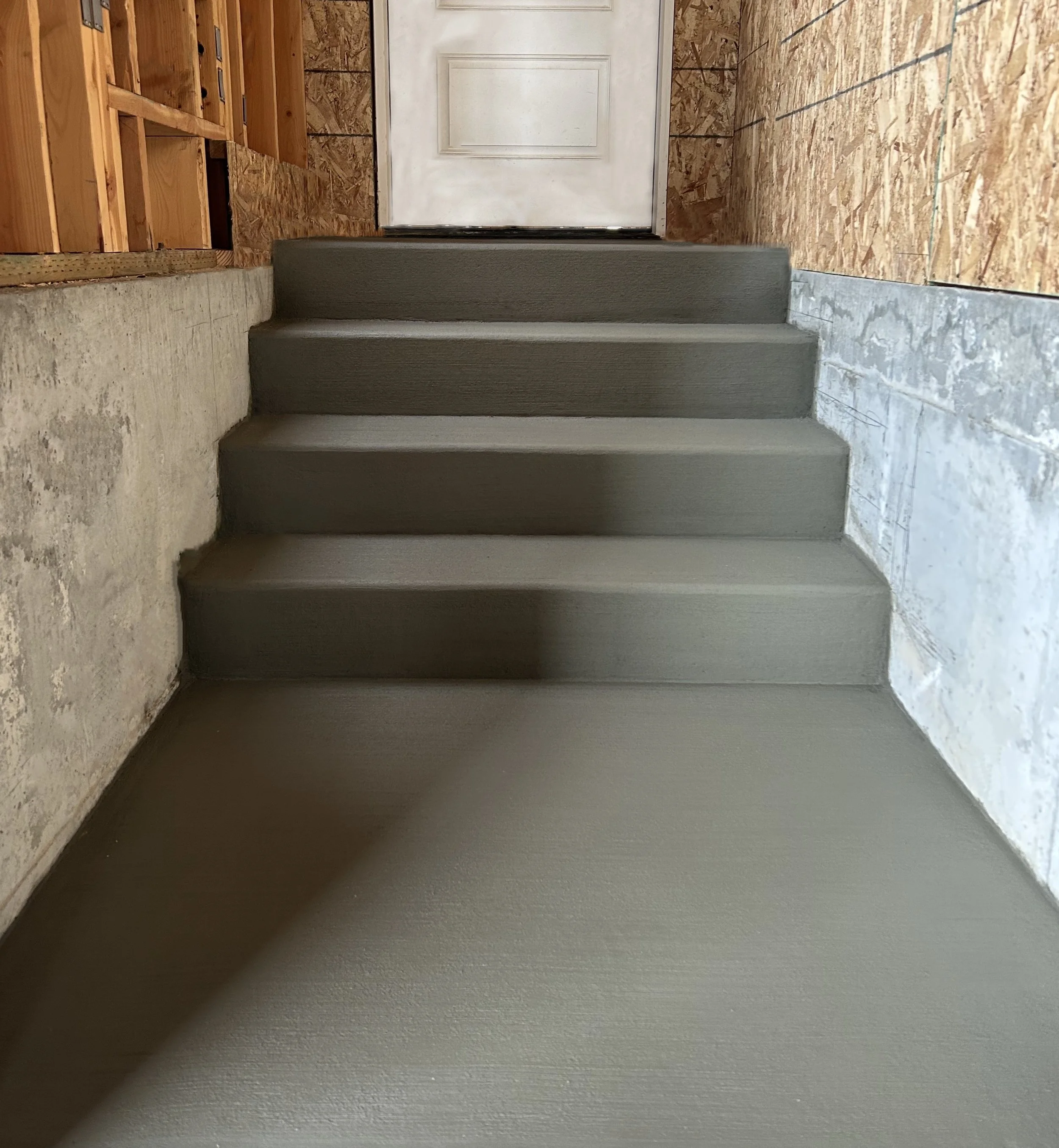 Newly painted staircase with gray paint, leading to a white door at the top. Construction materials and unfinished walls are visible on the sides.