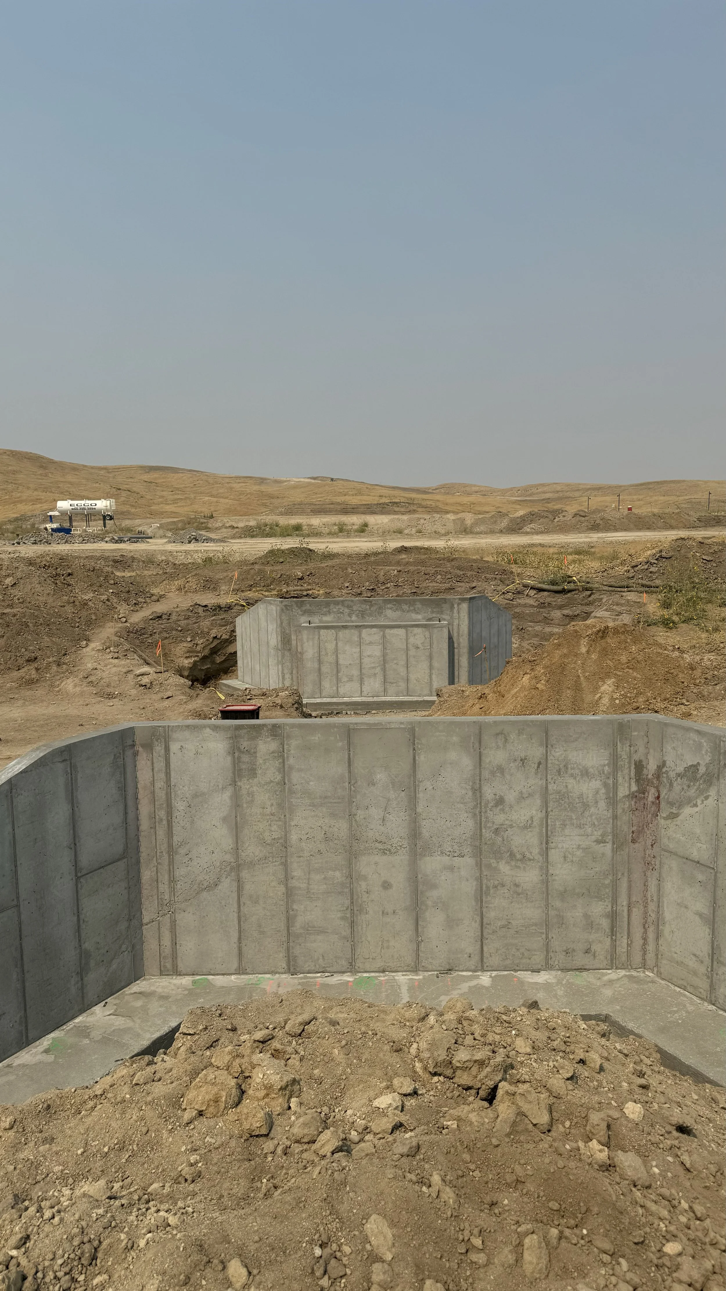 Construction site with concrete structures in a dry, hilly landscape under a clear blue sky.
