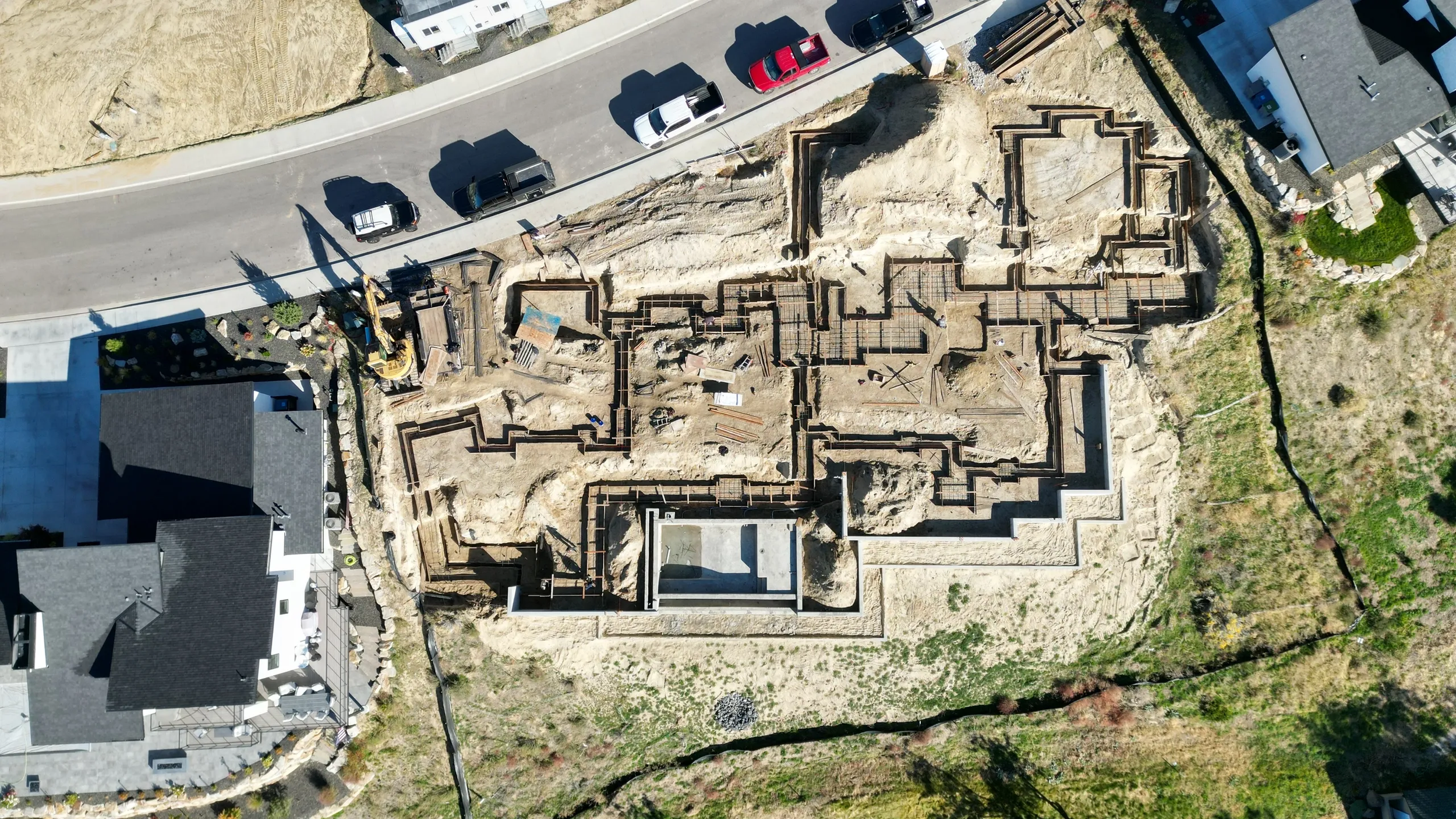 Aerial view of a construction site showing the foundation of a building being laid, with excavation and construction materials around.