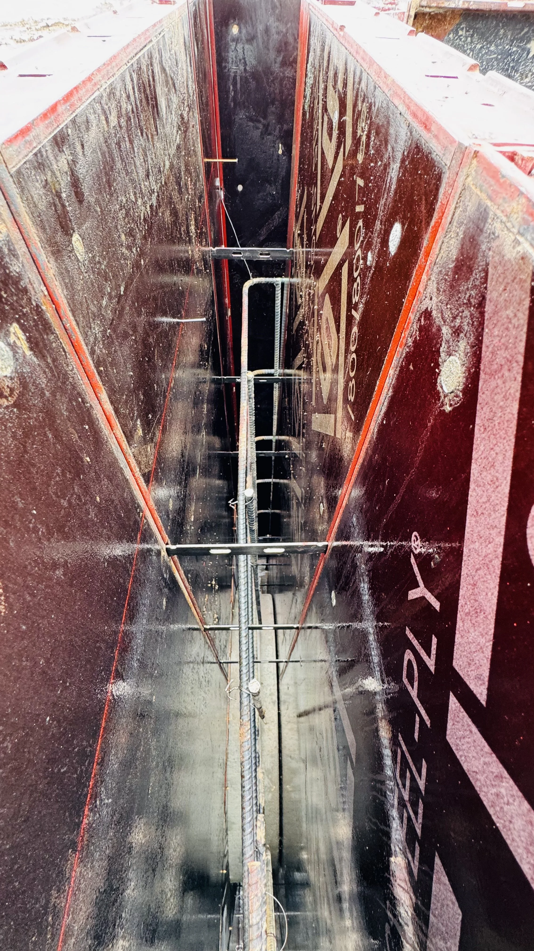 Inside a large metal bin or container, showing structural supports, wiring, and markings, with a black interior